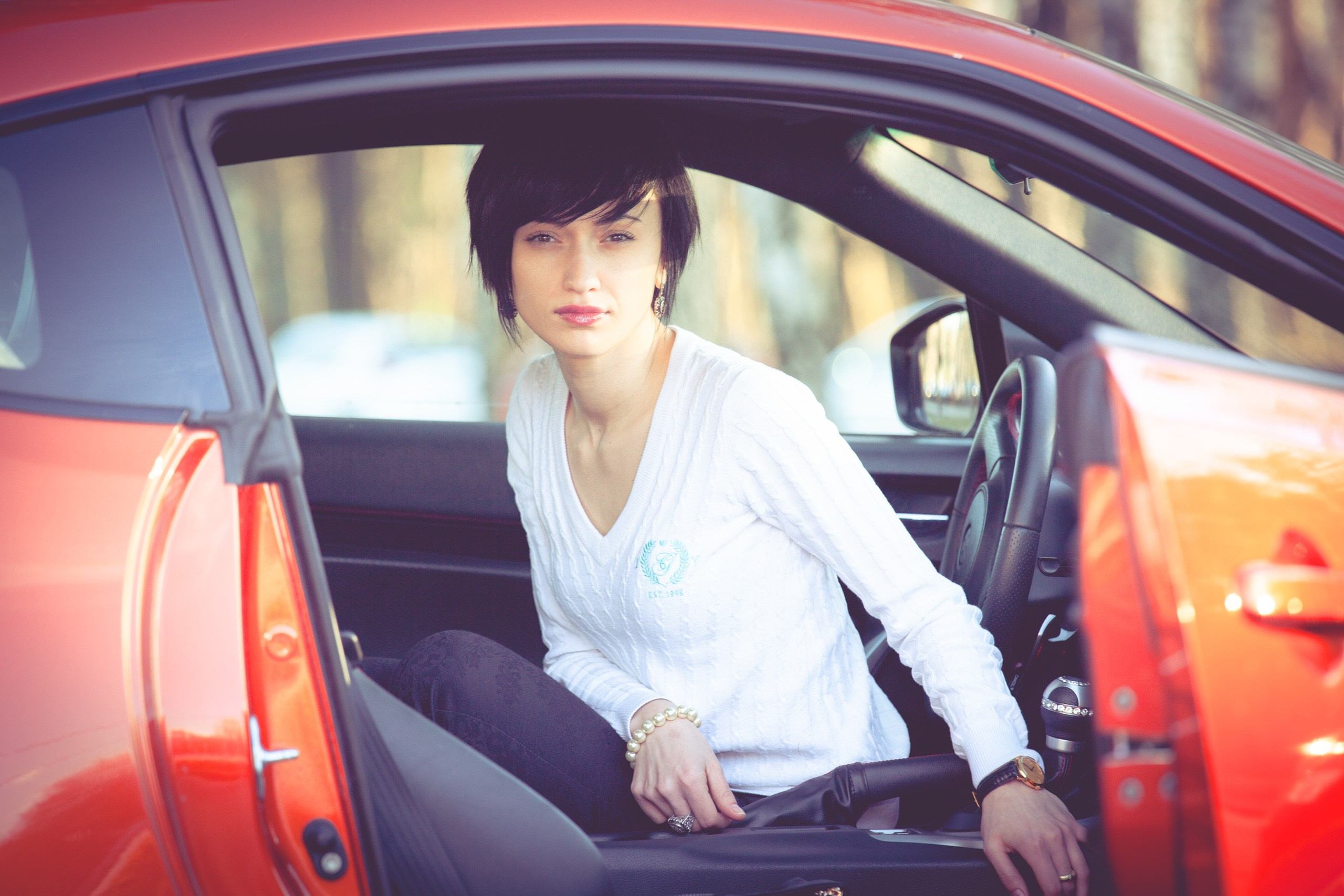 Девушка в элегантном пальто сидит за рулем современного автомобиля, сочетая классический стиль и динамичную жизнь.