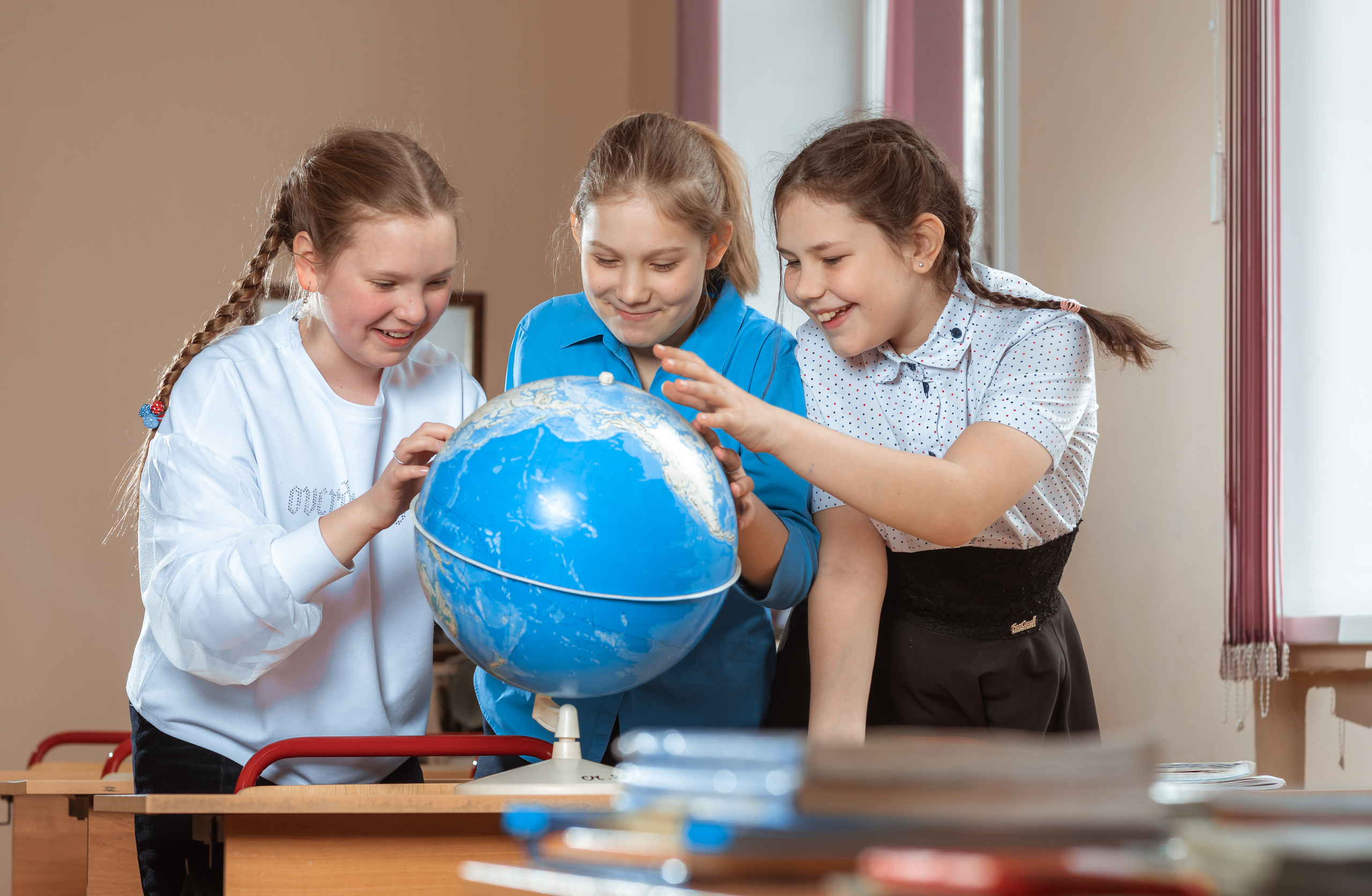 Три девочки изучают глобус в школьном классе