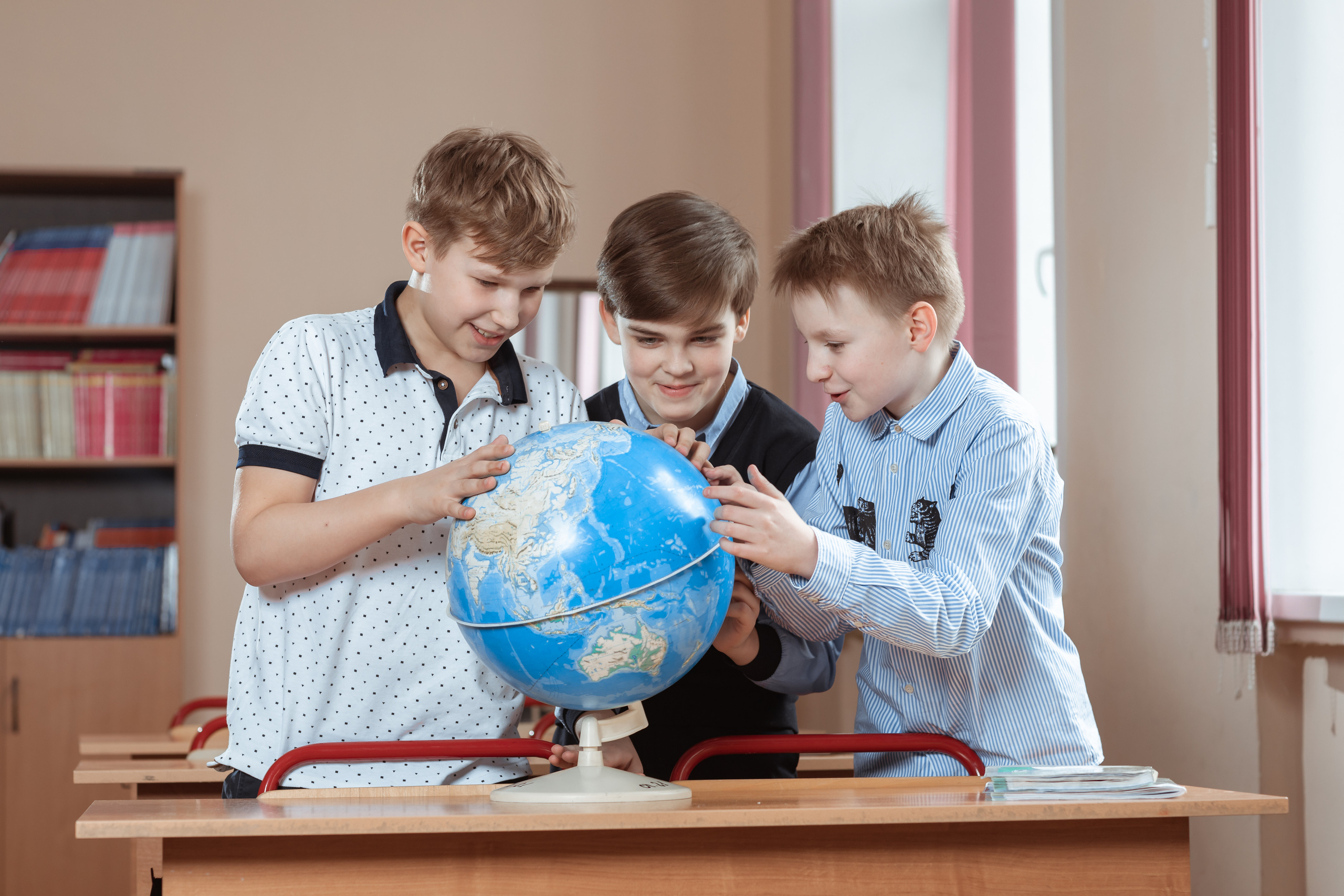 Три мальчика изучают глобус в классе