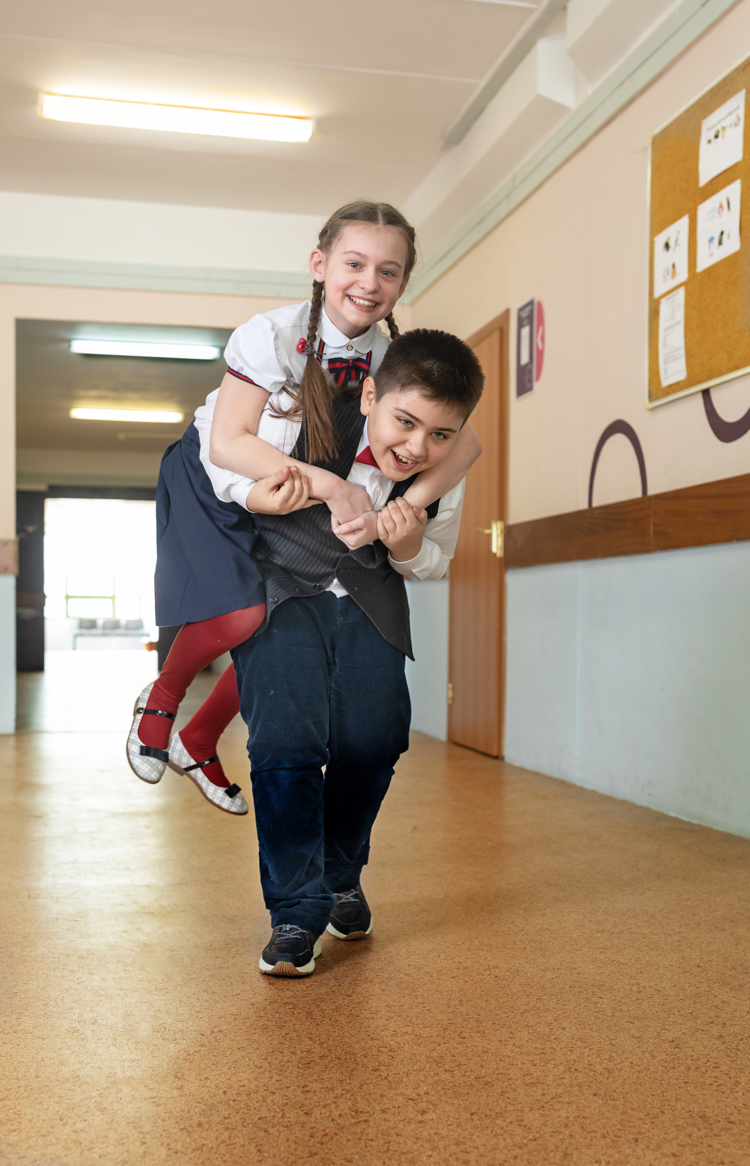 Девочка сидит на спине мальчика в коридоре школы