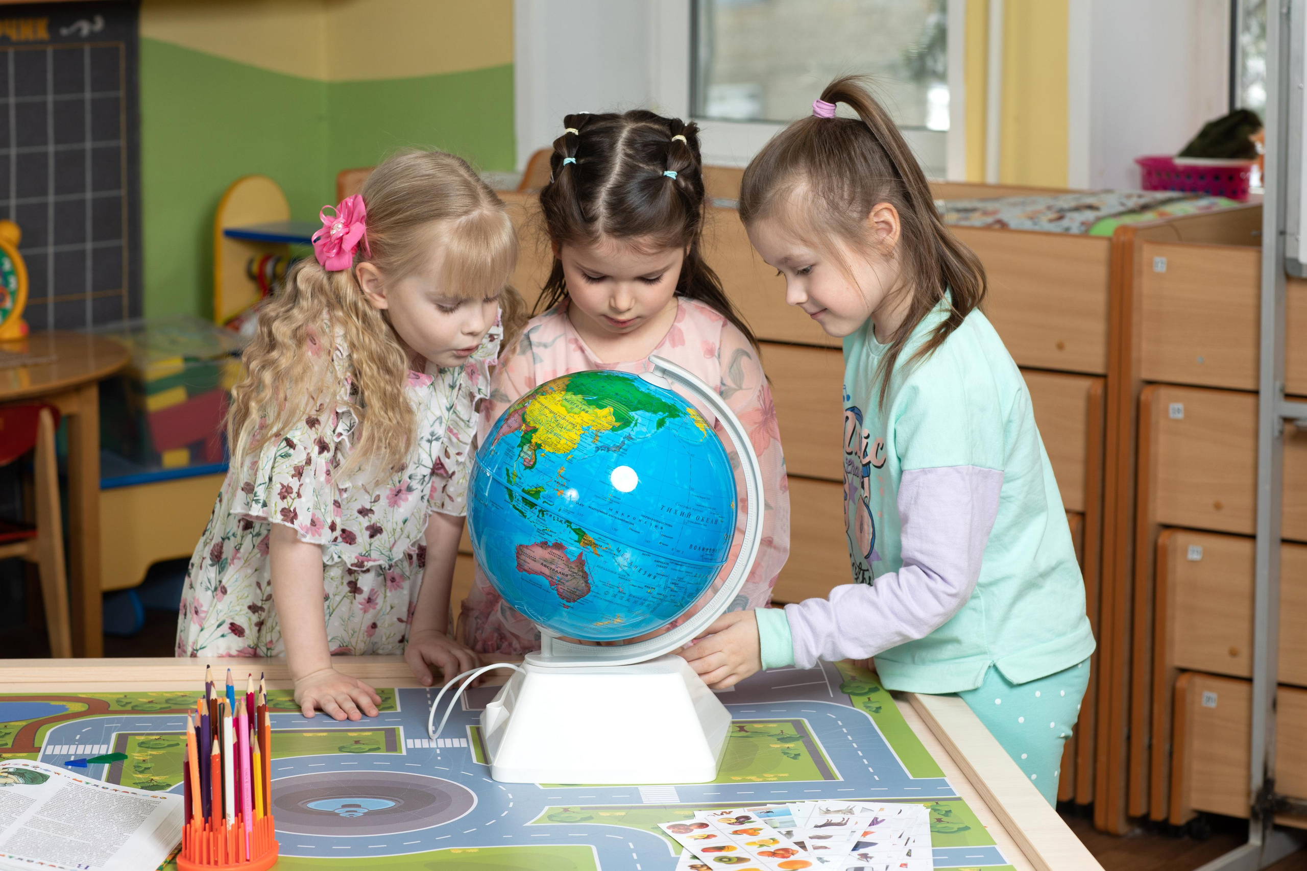 Три девочки изучают глобус в детском саду.