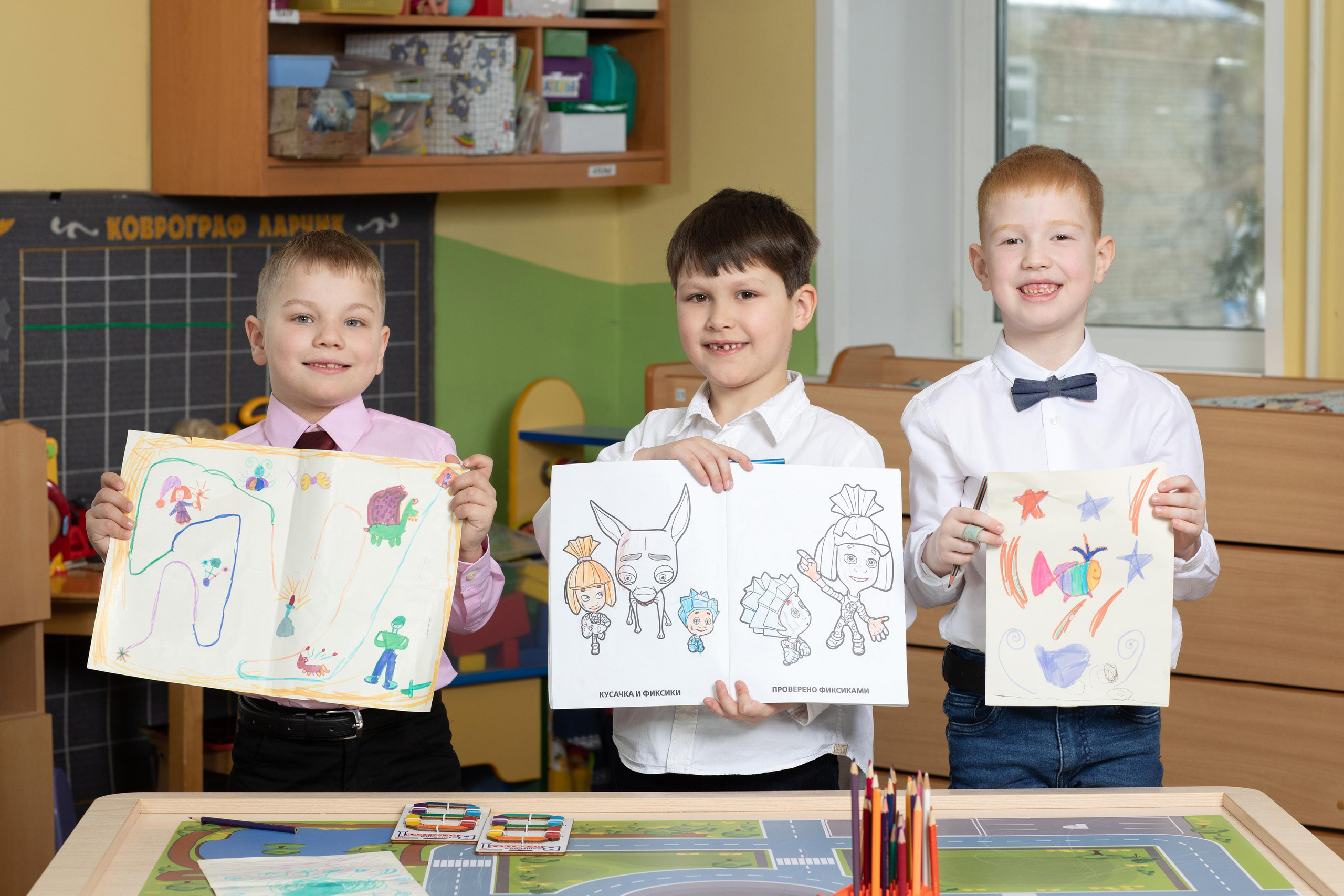 Мальчишки в детском саду показывают свои рисунки