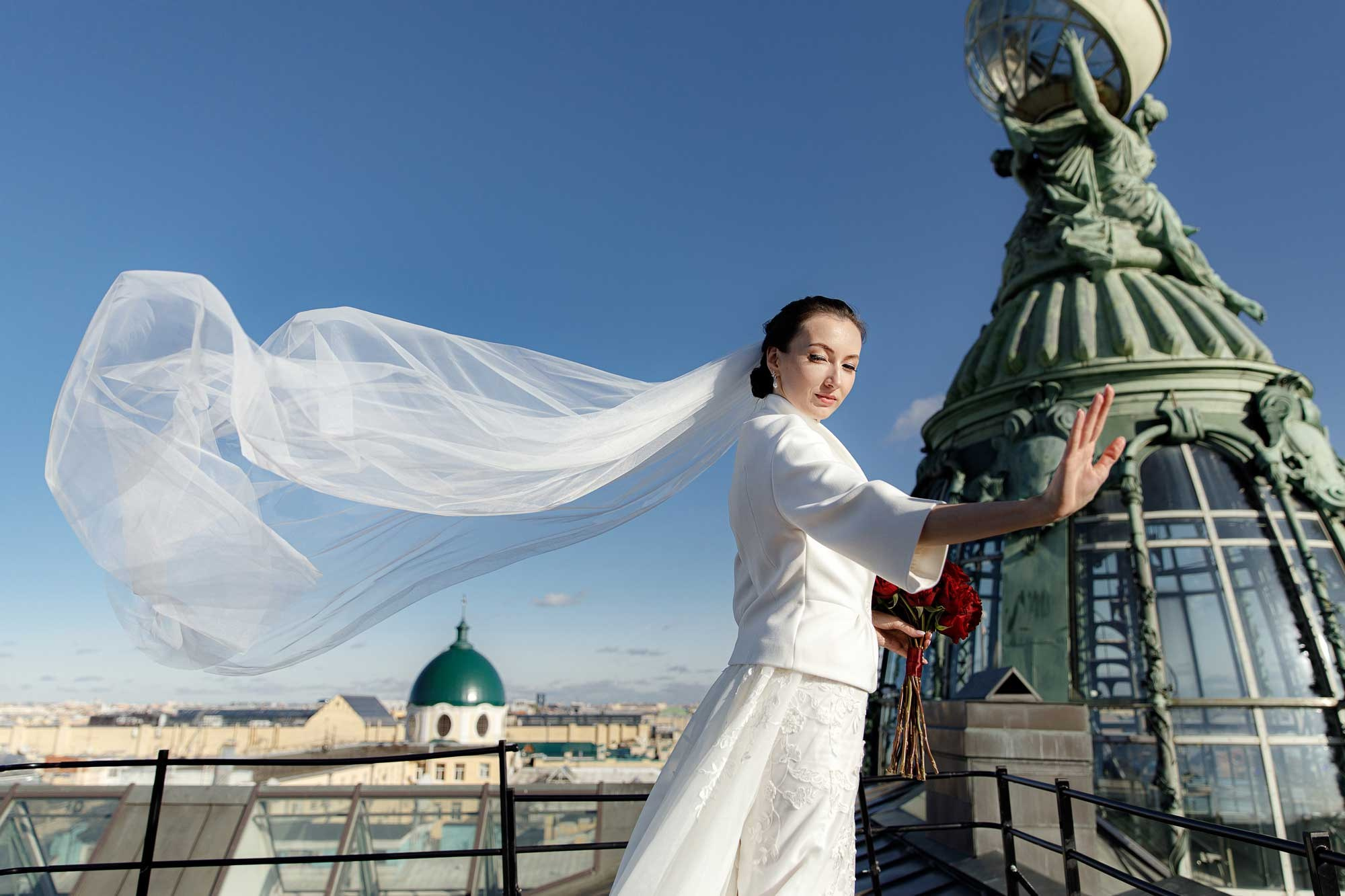 Невеста с развивающейся фатой стоит на крыше Дома Зингер
