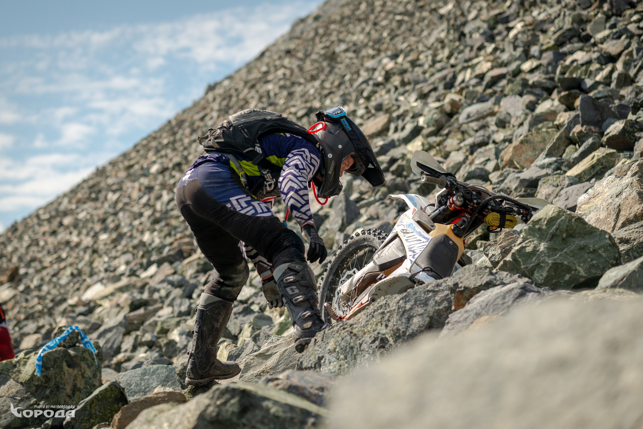 Мотоциклист в полной экипировке среди валунов, мотоцикл застрял.