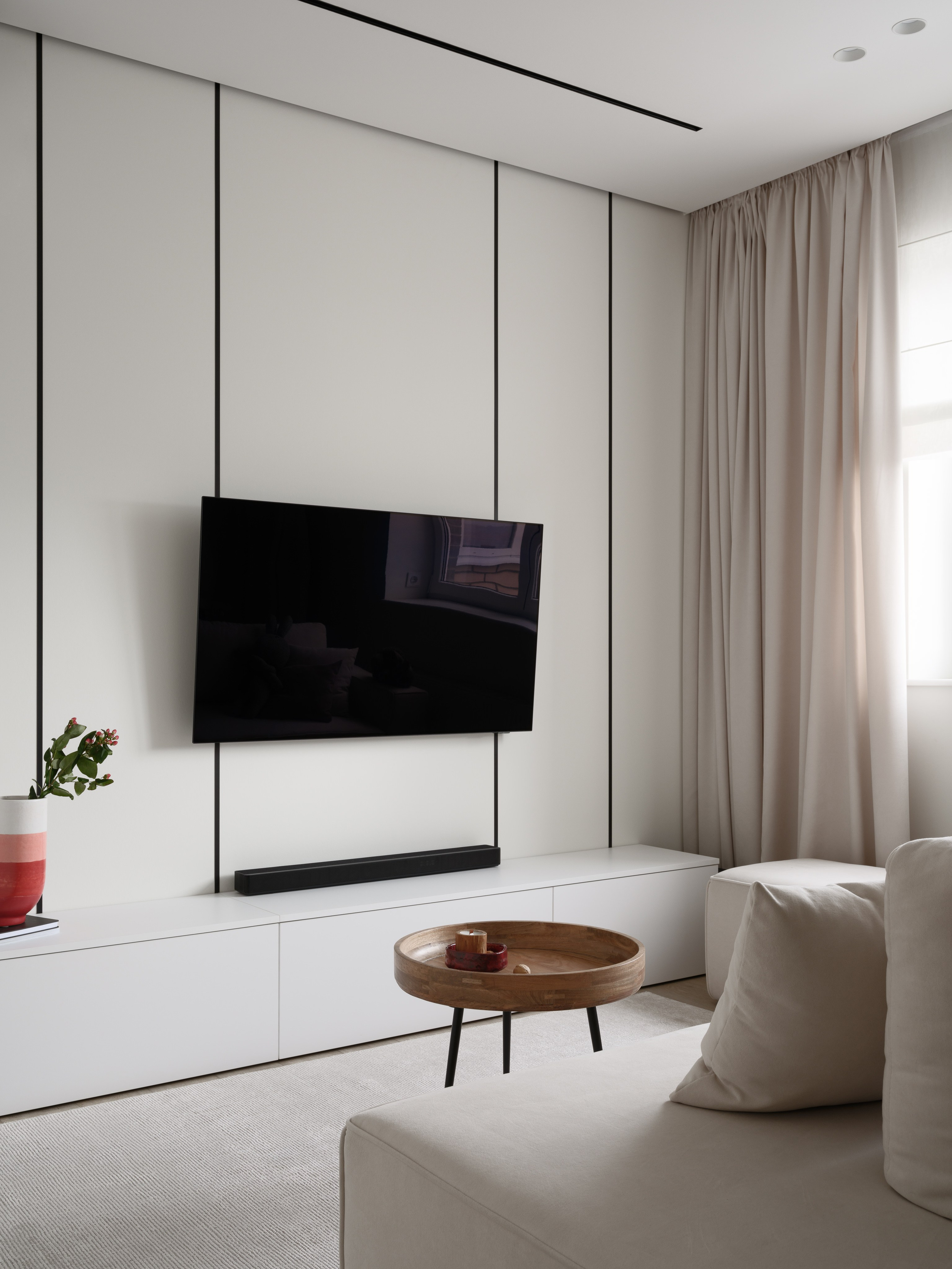 Минималистичная гостиная с телевизором, белой тумбой и бежевым диваном. Современный интерьер от дизайнеров Евгении Княжевой и Владлены Приваловой. Фотограф — Сергей Денисенко