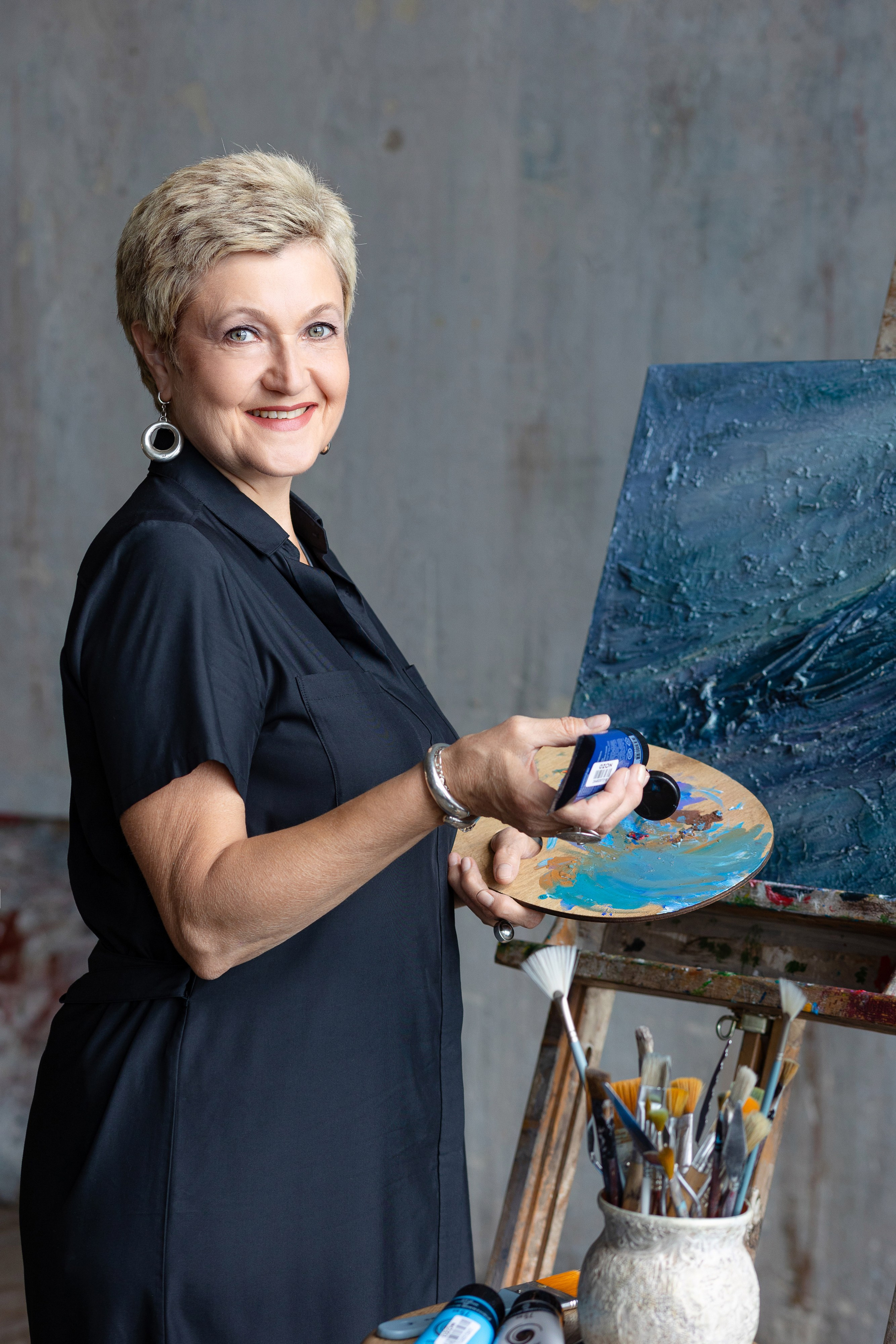 Художница с палитрой в руках стоит. улыбается в объектив