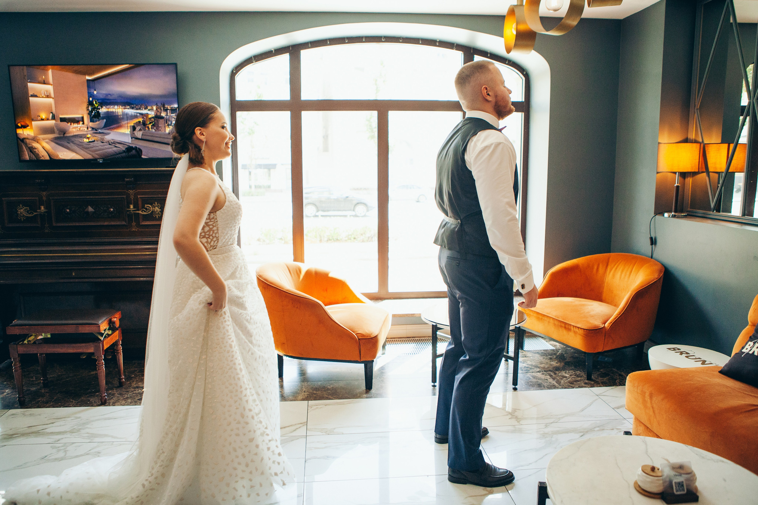 невеста подходит к жениху, первая встреча молодоженов в фойе отеля с оранжевыми креслами