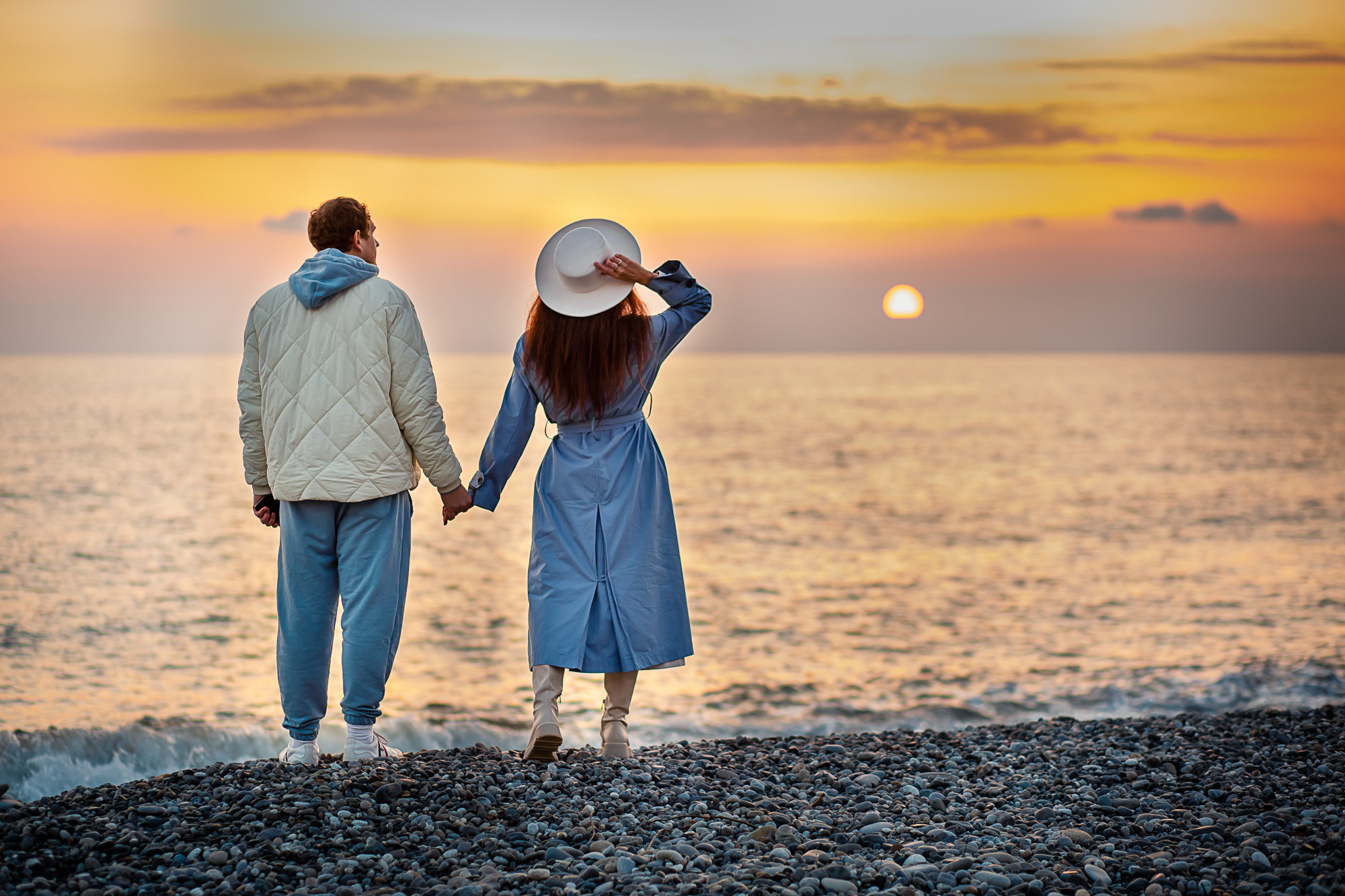 На закате муж и жена держатся за руки на берегу моря  
