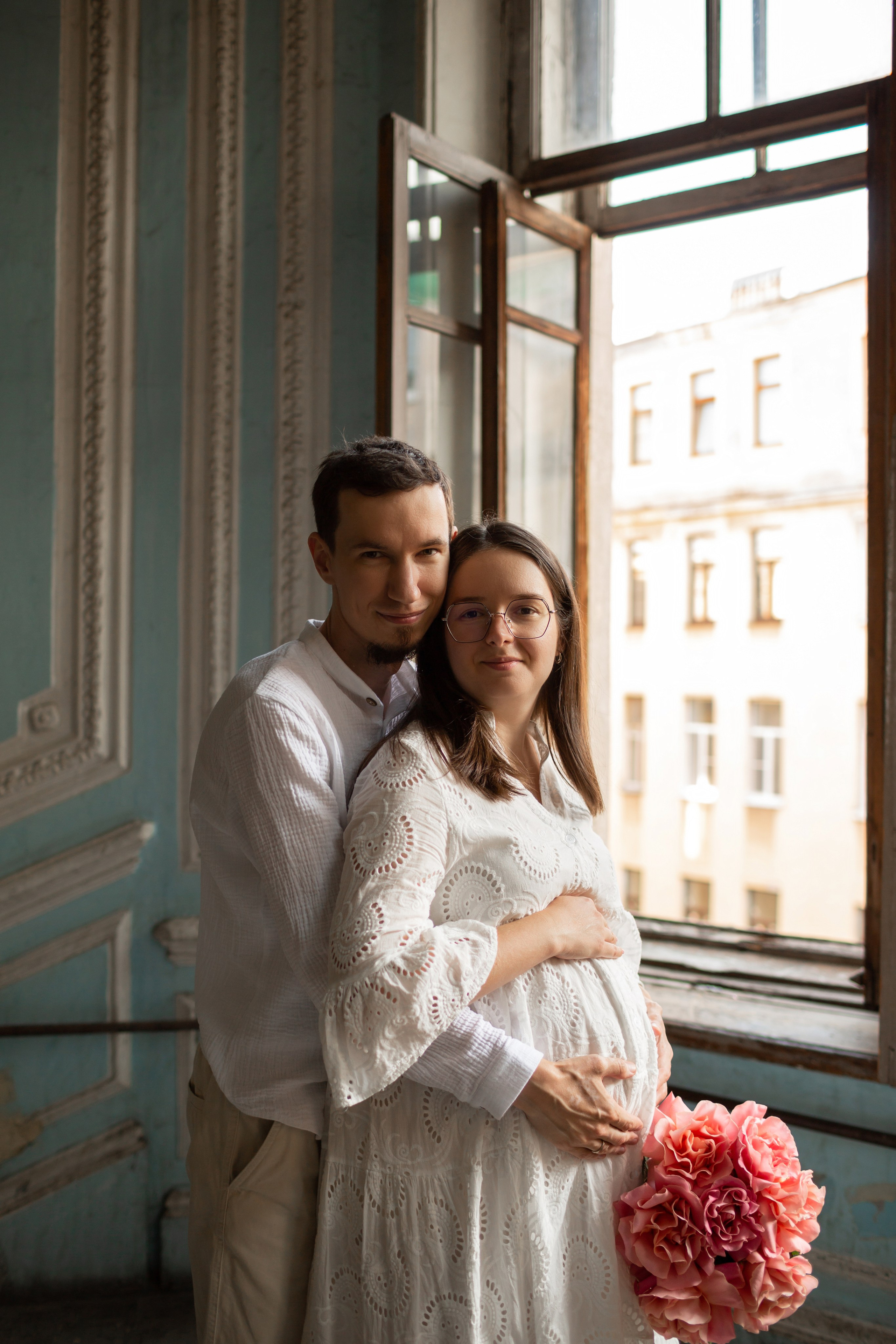 Муж обнимает беременную жену в старом дворе.