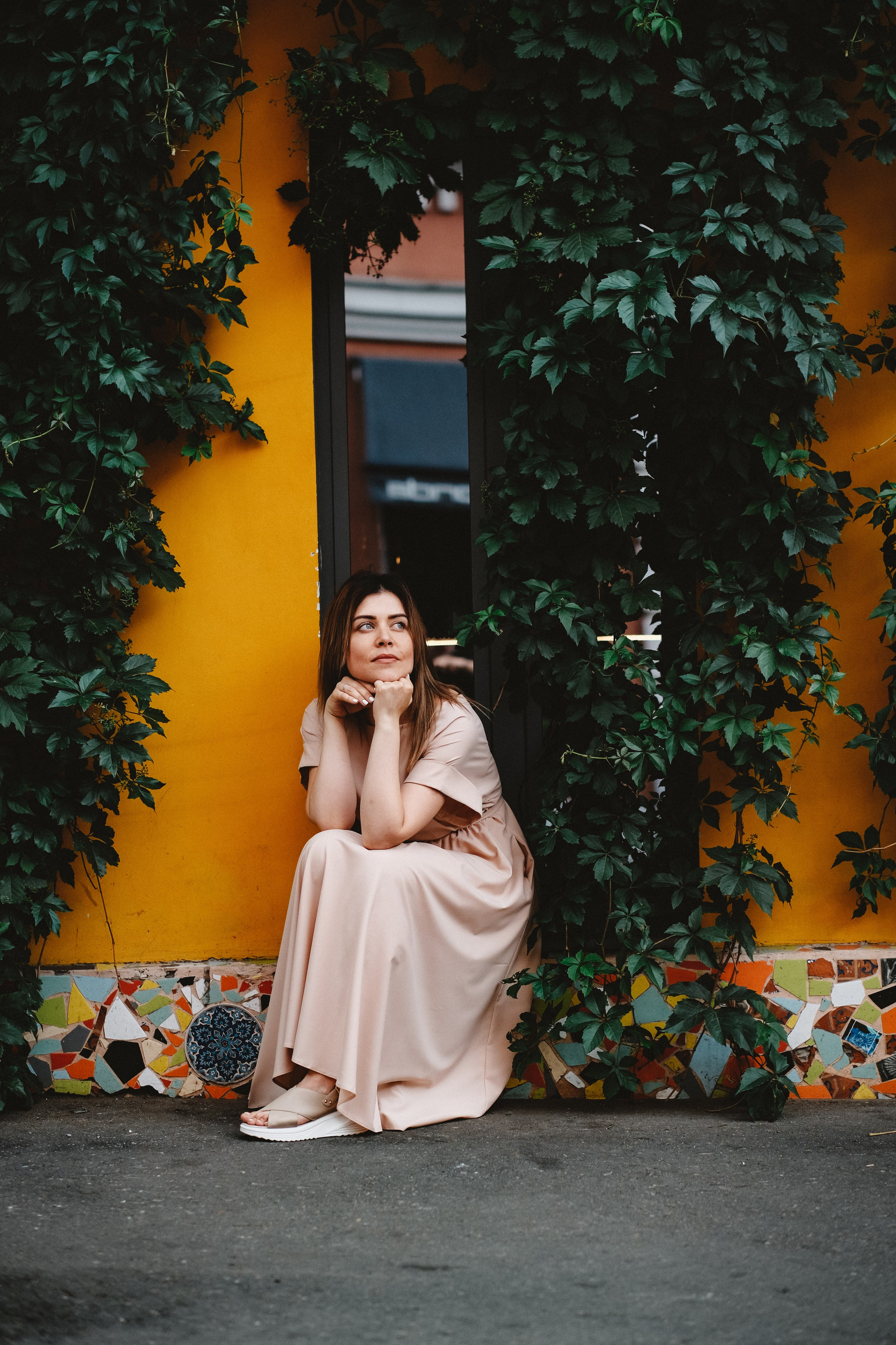 Девушка в окружении зелени на фоне желтого дома.