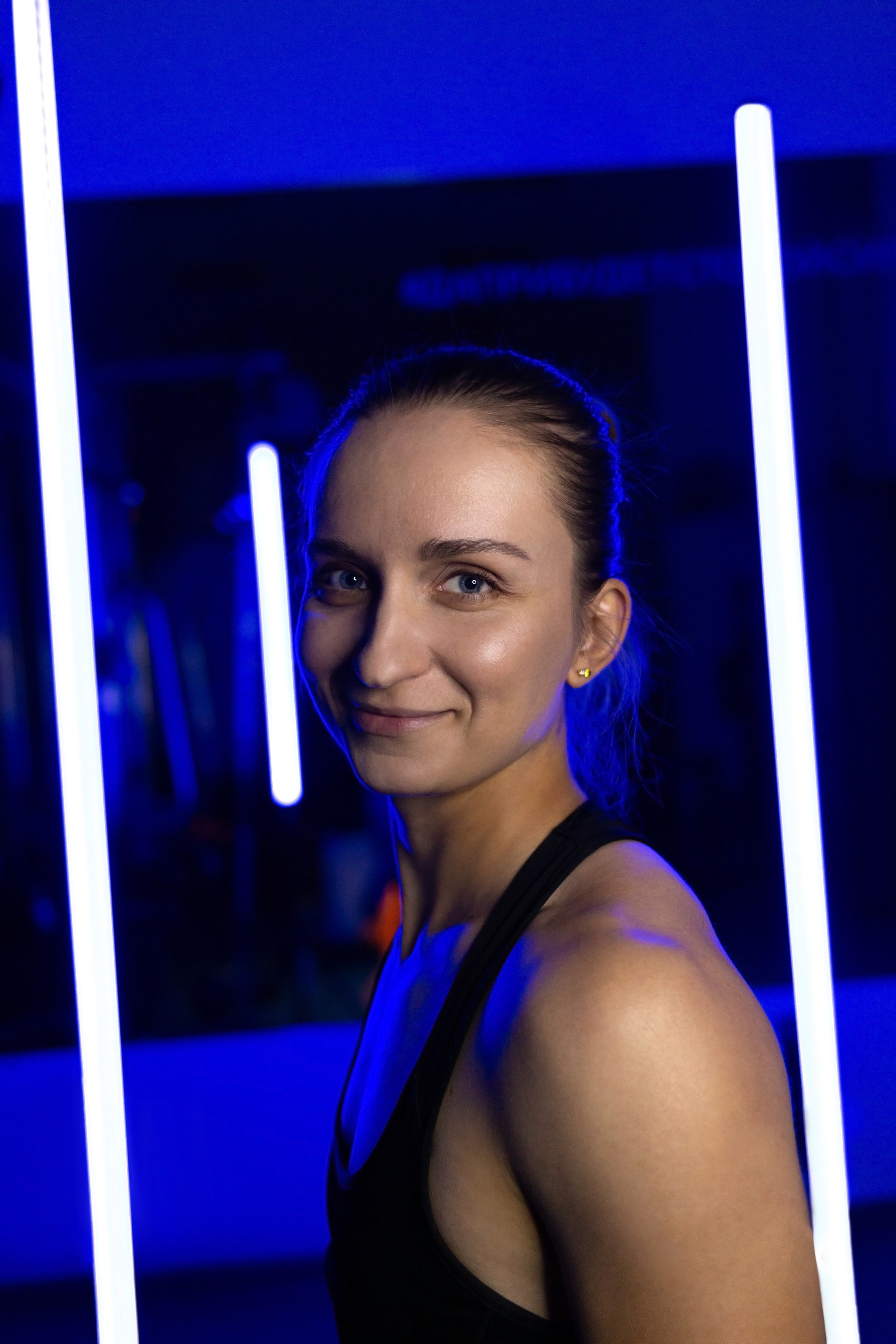 Женское лицо крупно с синей подсветкой. Девушка улыбается в свете синих неоновых ламп. Фитнес клуб Life Воронеж.