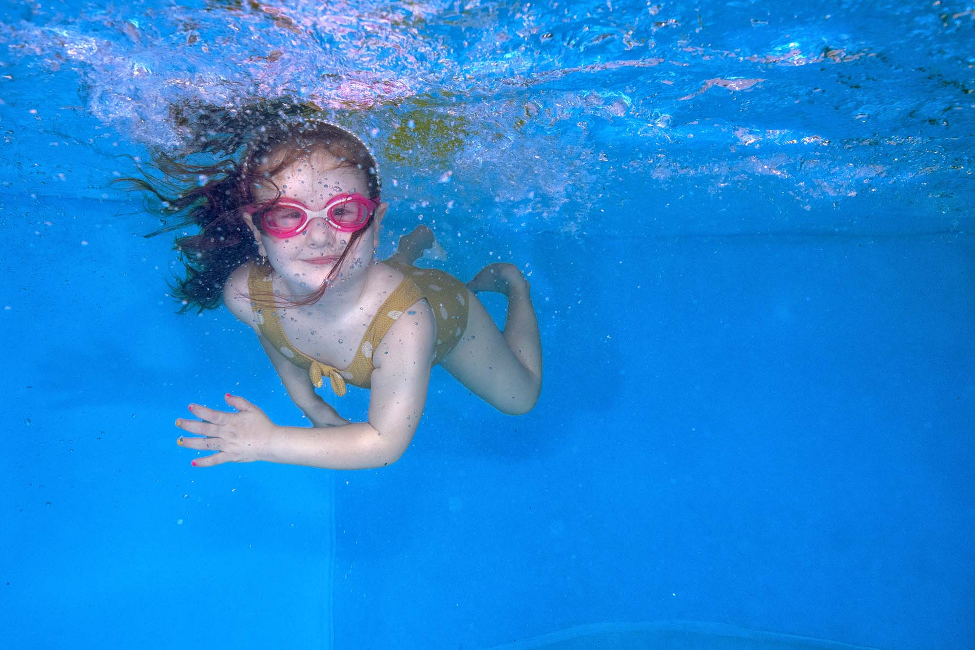 Маленькая девочка плывет под водой и смотрит в камеру.  Детский фитнес