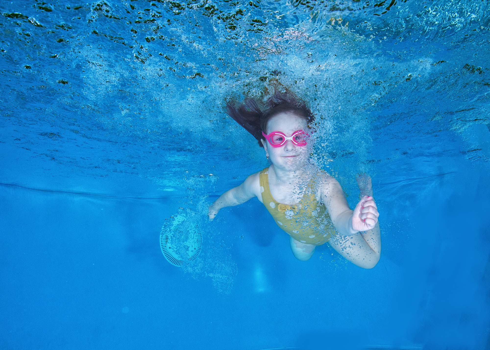 Маленькая девочка плывет под водой очень довольная, вокруг нее много пузыриков. отдых с детьми бассейн