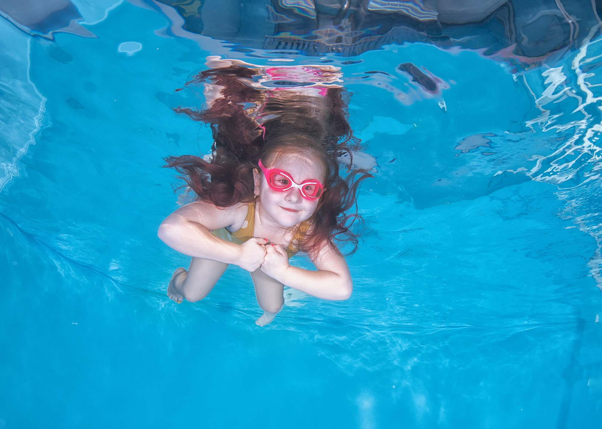 Маленькая девочка лежит на воде и смотрит вниз. Как научить ребенка плавать