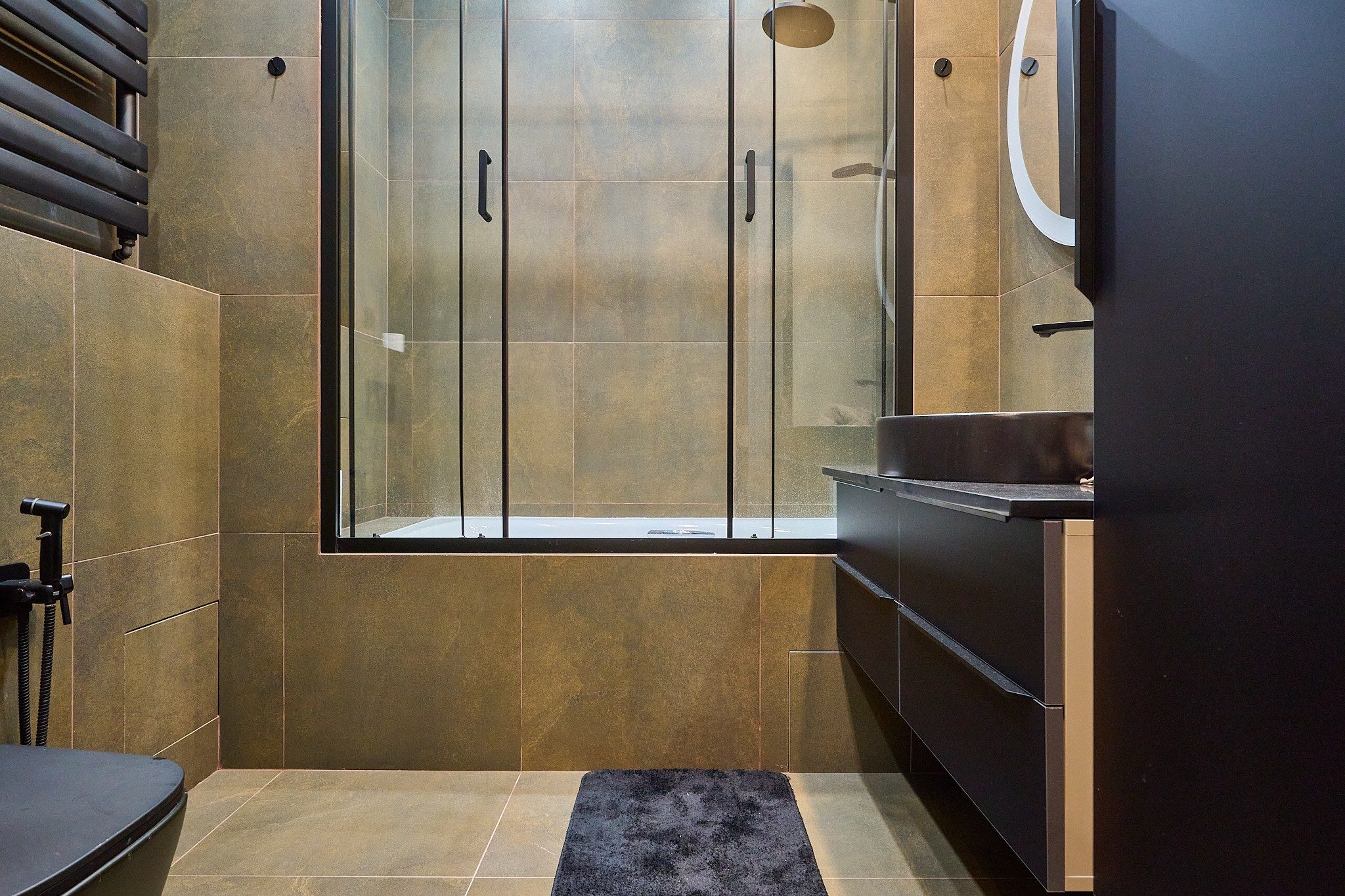 ванная комната с коричневыми плитами прозрачной душевой кабиной и черными шкафами 