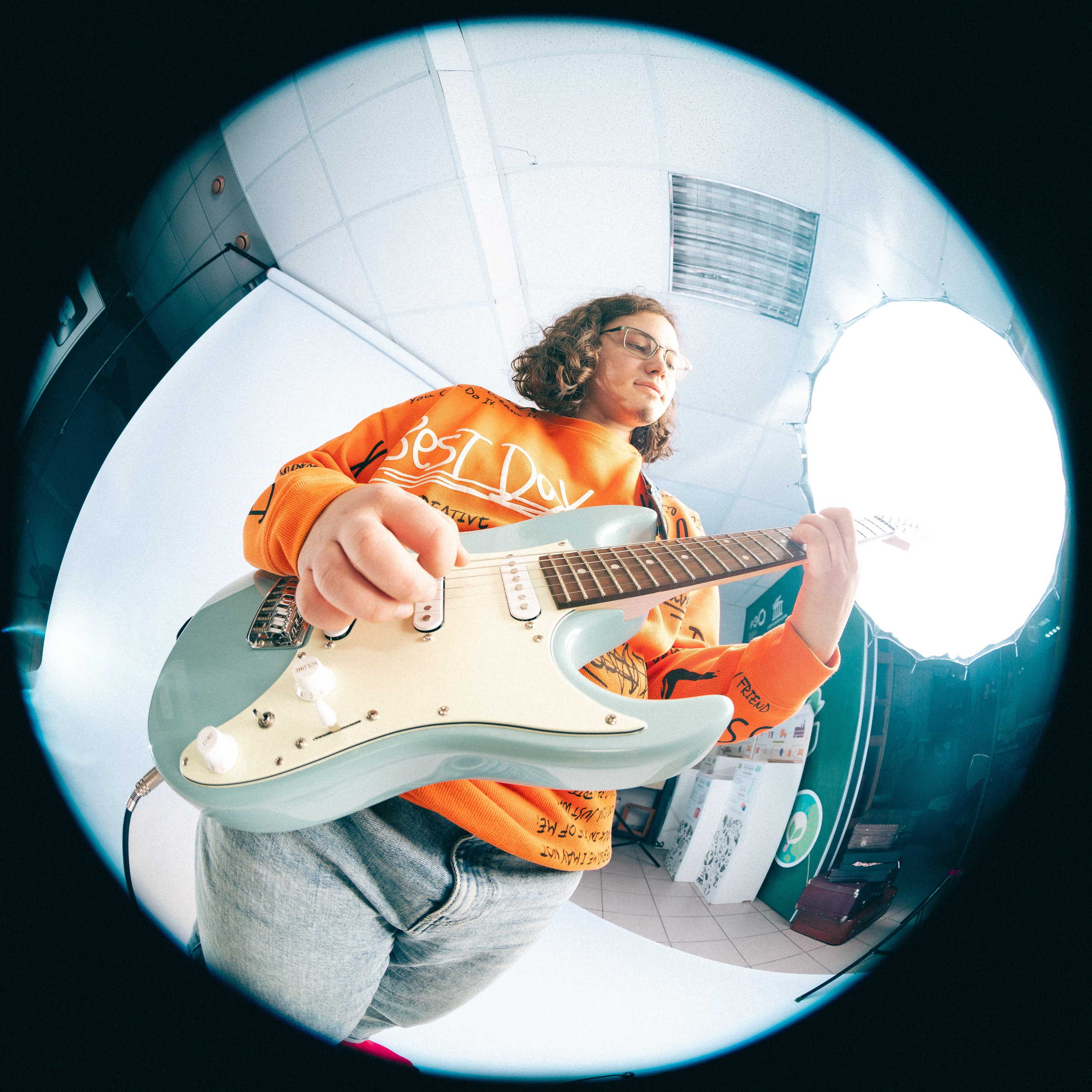 Молодой парень позирует в студии в яркой оранжевой одежде с гитарой