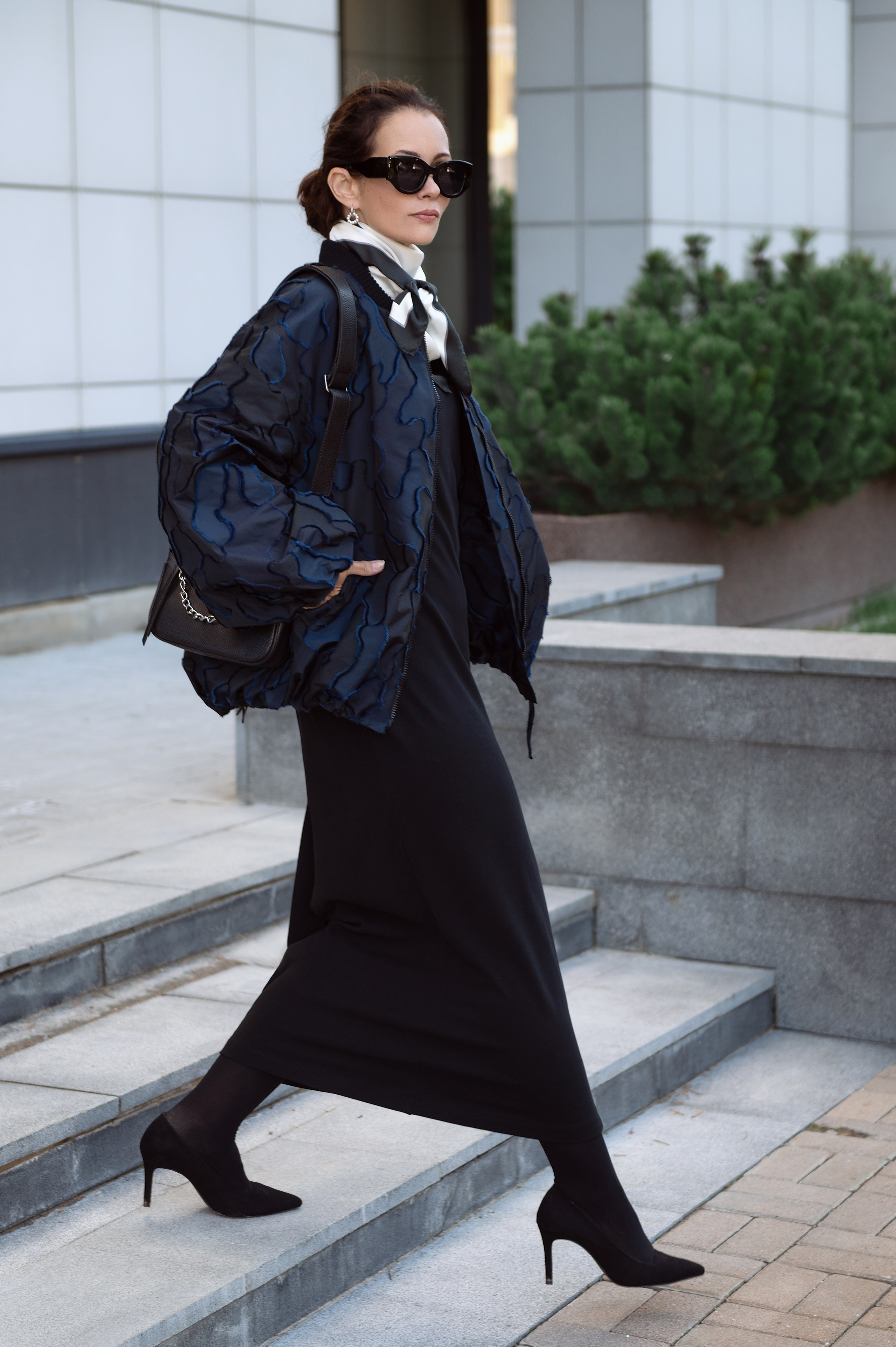 Девушка идет по лестнице, она одета в темно-синий бомбер, черное платье и шелковый платок. Съемка для магазина женской одежды и аксессуаров. Уличная съемка