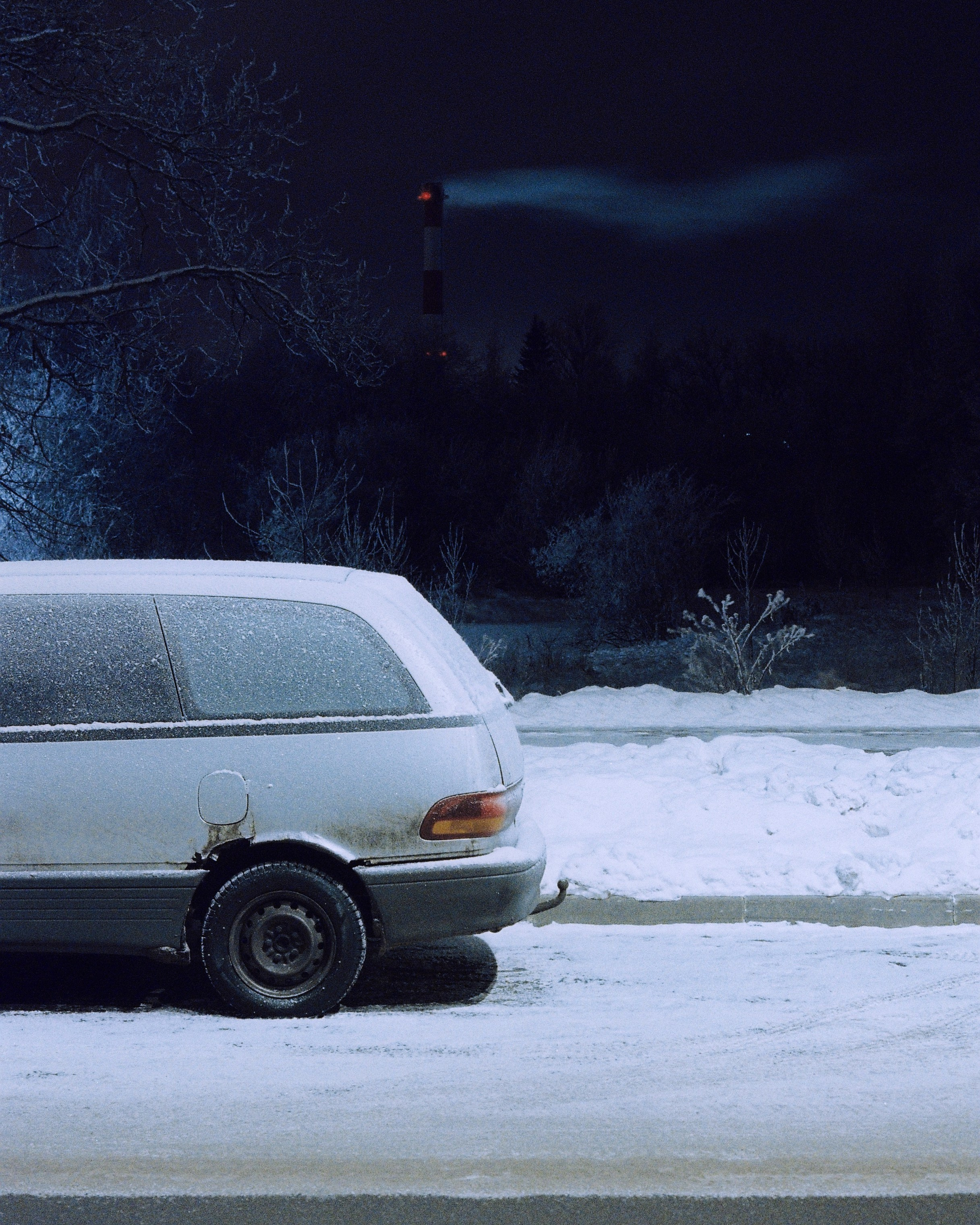 Припаркованный одинокий минивэн на парковые на фоне темного морозного леса, ночной пейзаж.