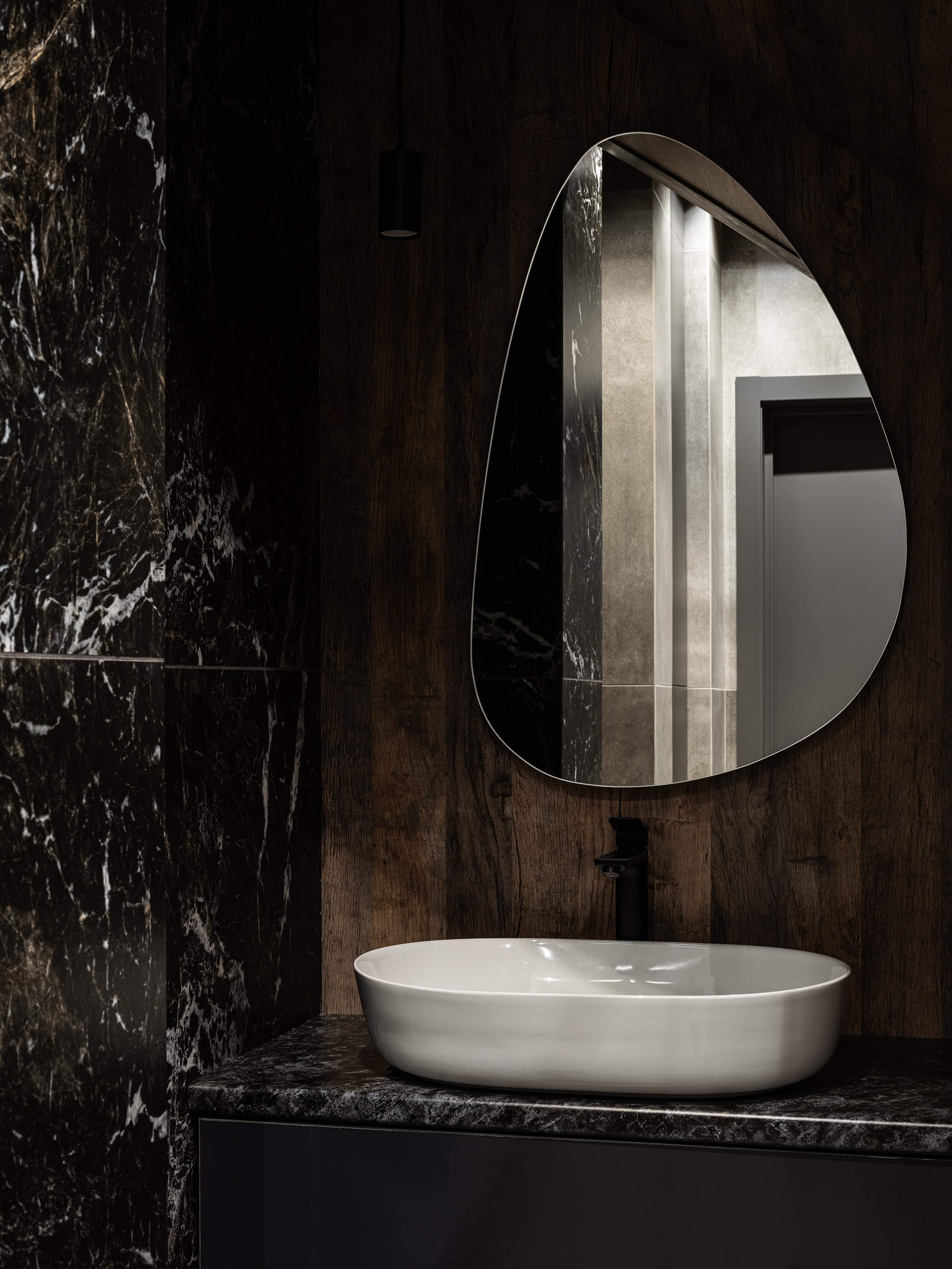 Дизайнерский умывальник с белой овальной раковиной, асимметричным зеркалом и черным смесителем на фоне стен из дерева и мрамора; стильный санузел от Екатерины Мищенко, съемка фотограф Сергей Денисенко.