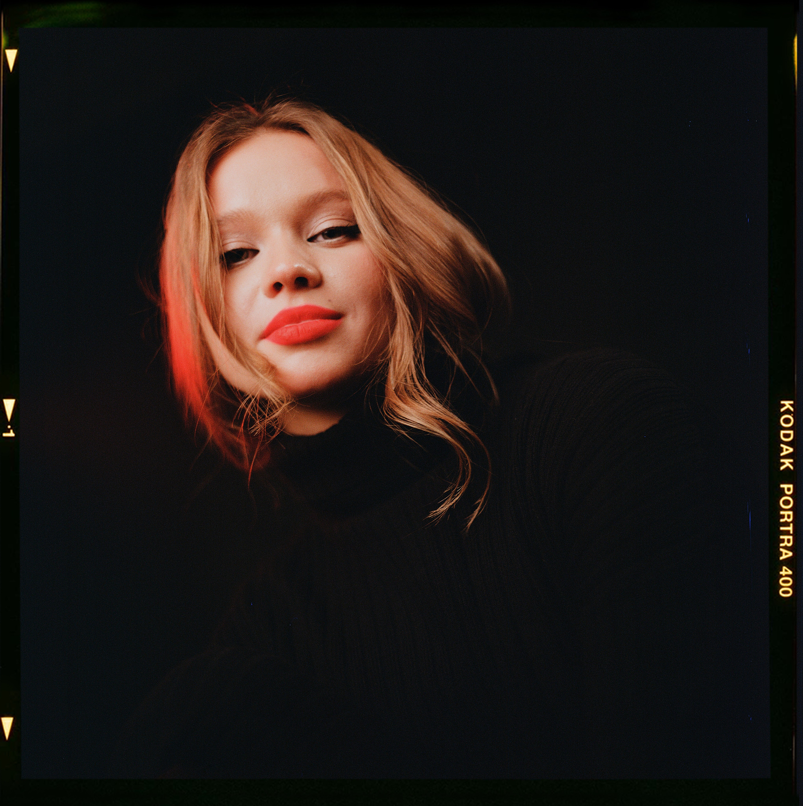 Красивая девушка славянской внешности с красными губами на черном фоне смотрит в камеру на фотосессии