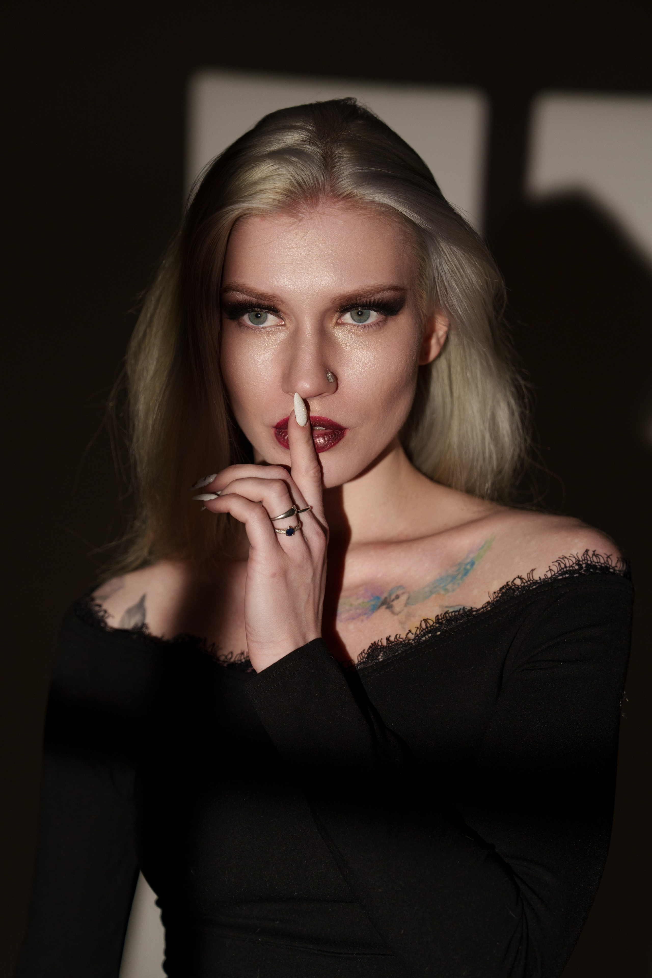 блондинка в черном платье смотрит в окно с задумчивым взглядом