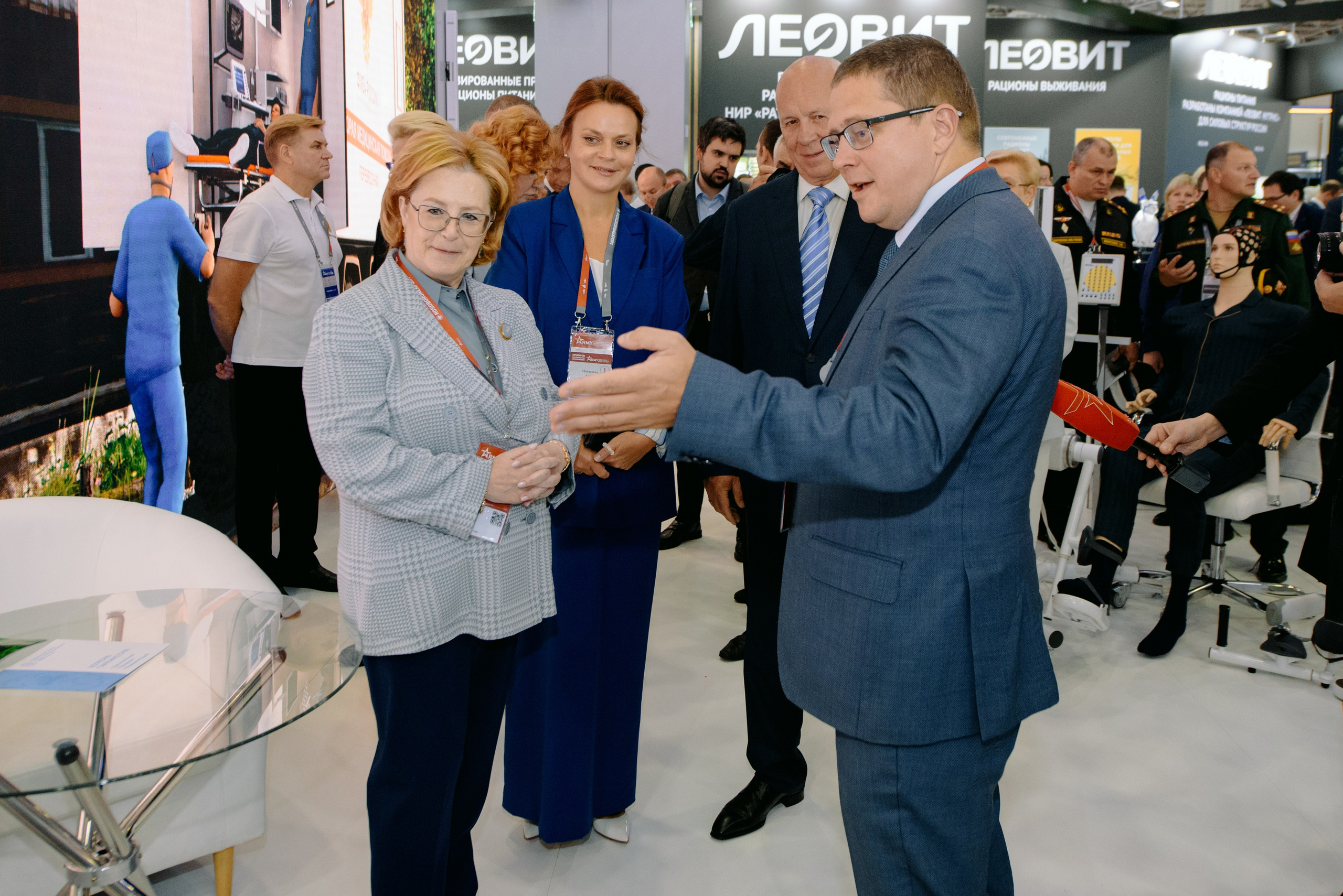 Фотография с выставки, на которой изображены участники, обсуждающие экспонаты.  Фотография репортажного характера, запечатлевшая важный момент корпоративного мероприятия. Министр обороны РФ Белоусов. Чемезов Роснано. Армия 2024. Вероника Скворцова