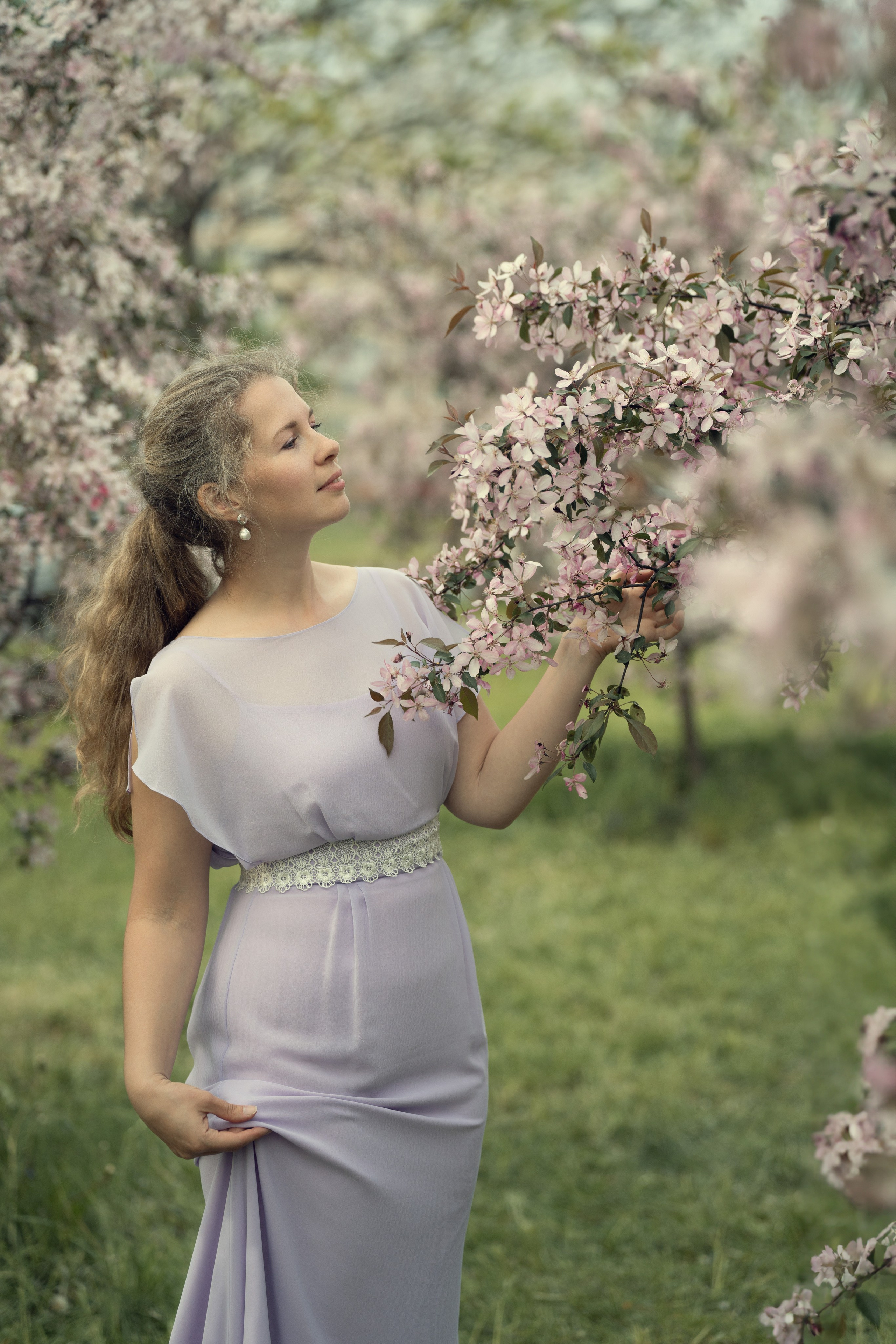 Женский портрет в цветении в яблоневом саду на семейной фотосессии. Девушка в нежно сиреневом платье