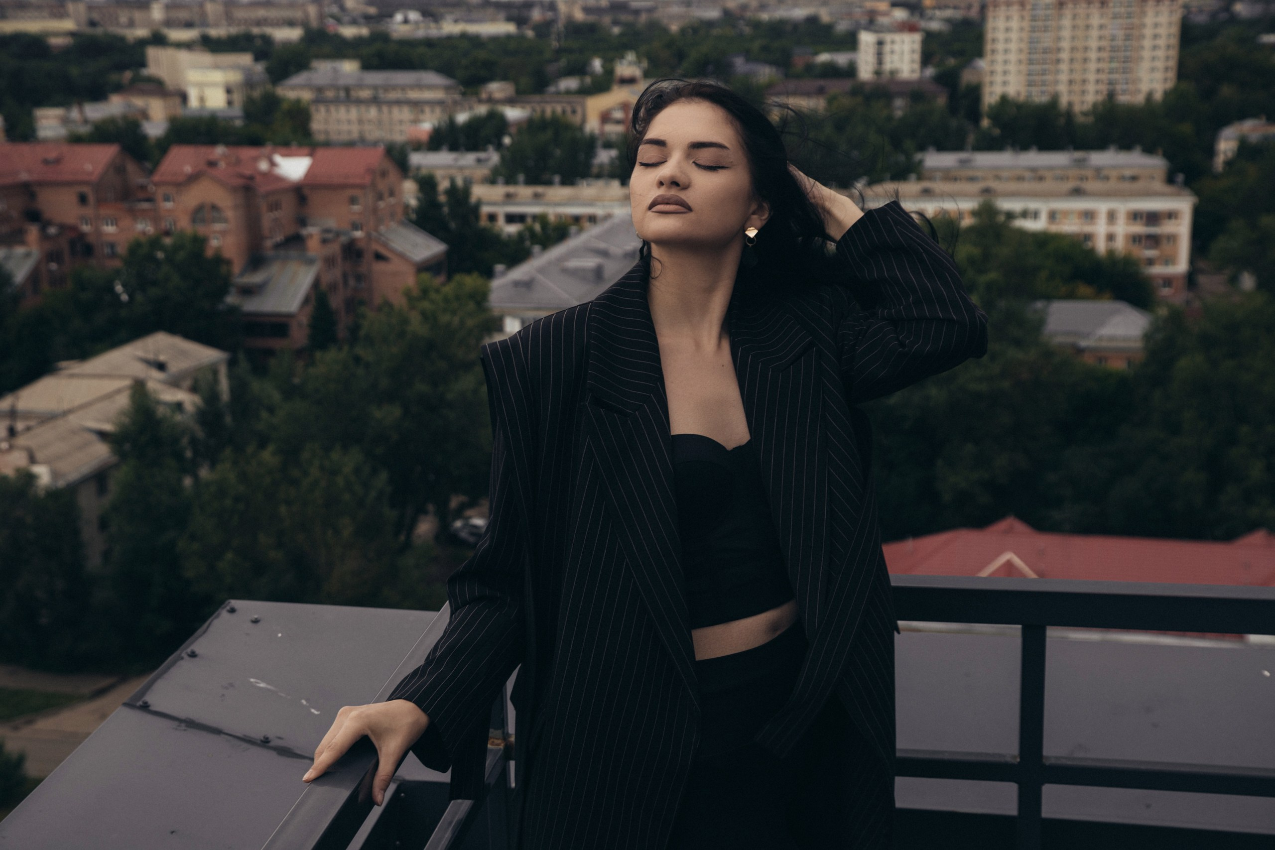 Девушка в черном костюме стоит на крыше. Модная фотосессия, городской пейзаж, портрет.