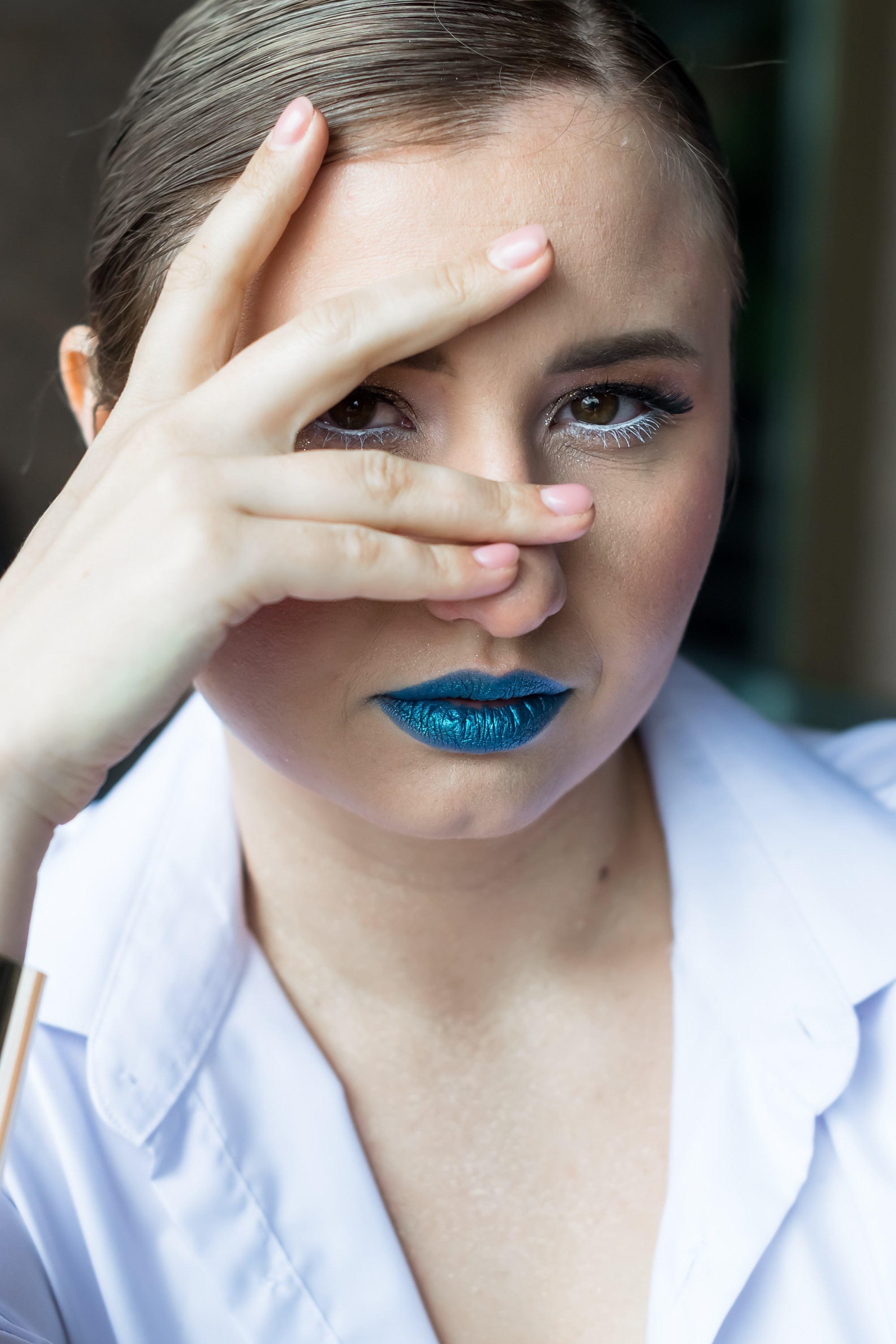 На фото девушка в белой рубашке закрывает рукой глаз.