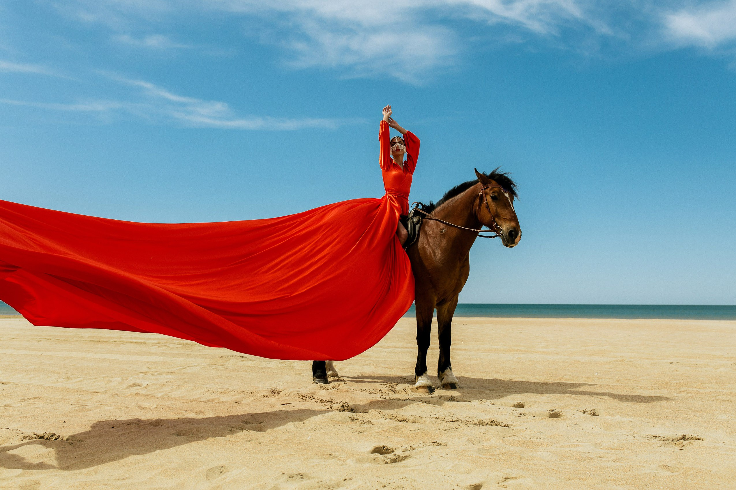 Девушка в платье с длинным шлейфом фотографируется верхом на лошади.