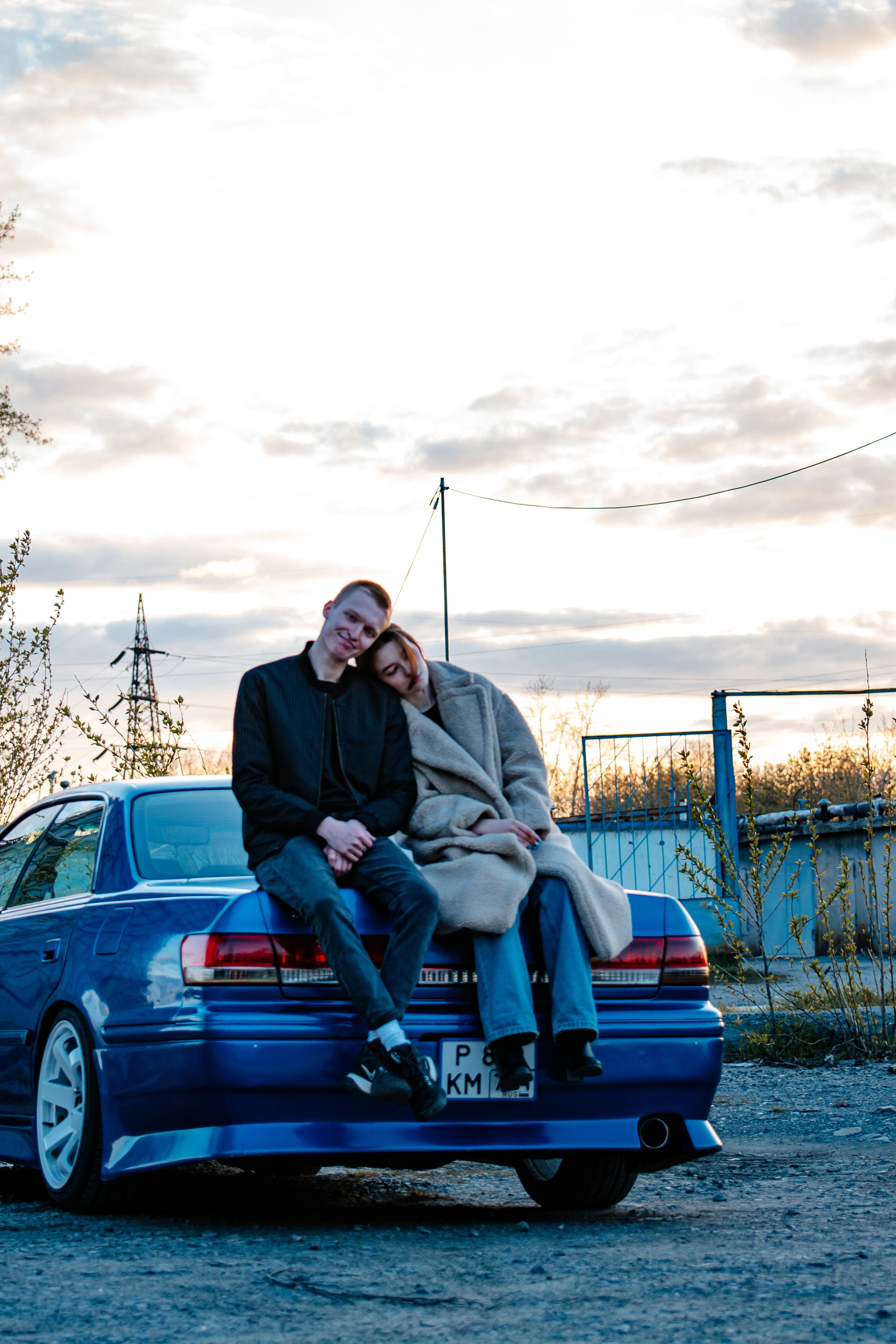 Парень и девушка опираются на машину на фоне заката
