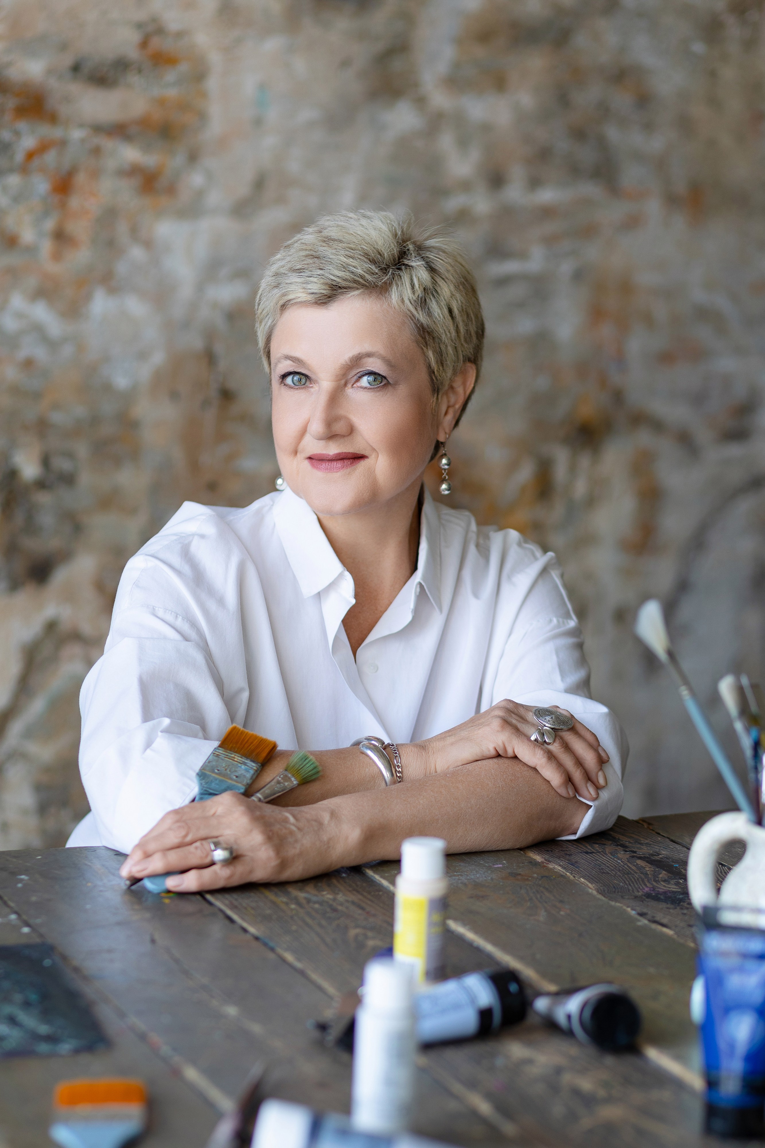 Художница сидит за столом на фоне раскрашенной стены.