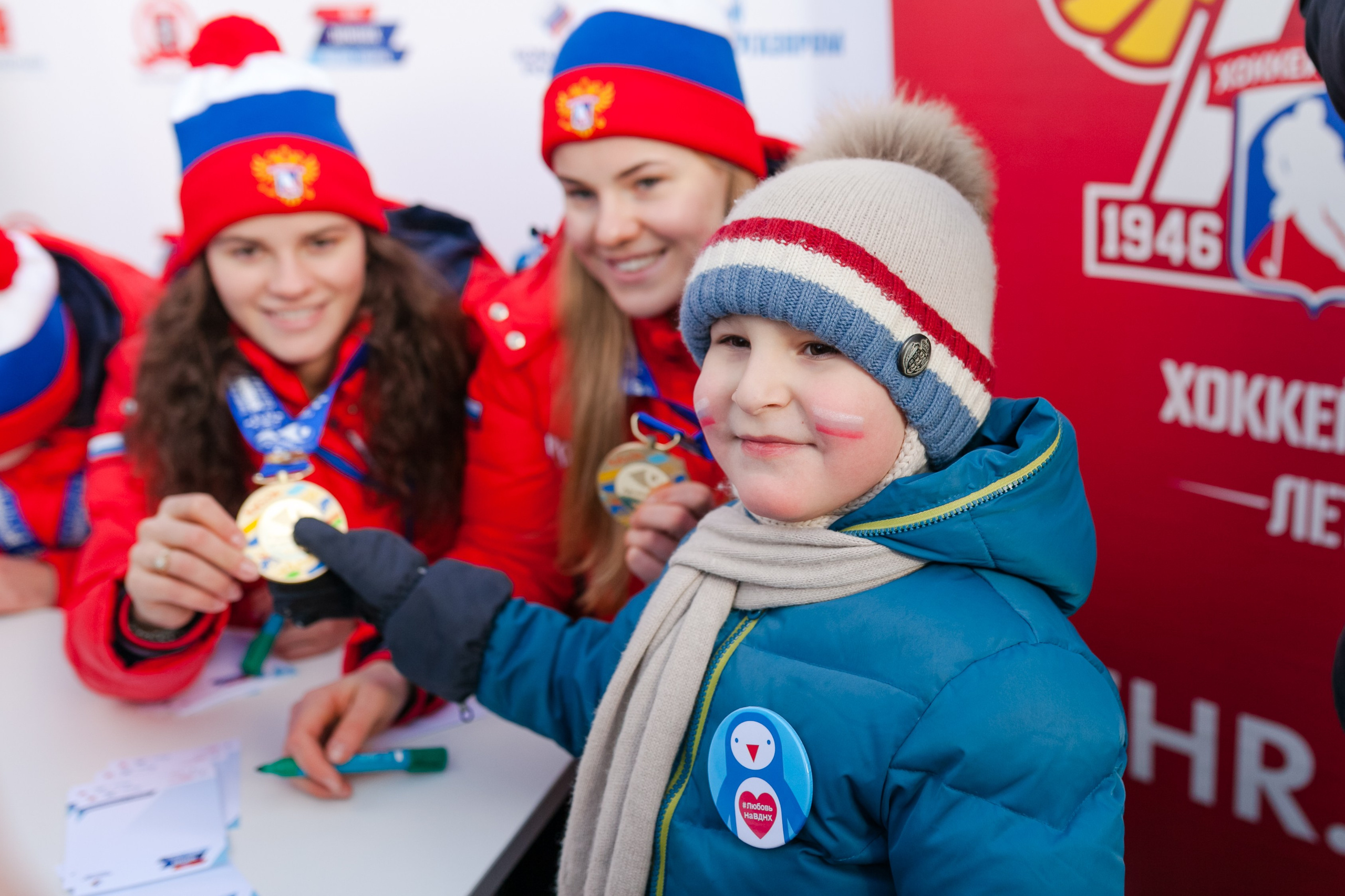 Маленький мальчик трогает золотую медаль у спортсменки на груди