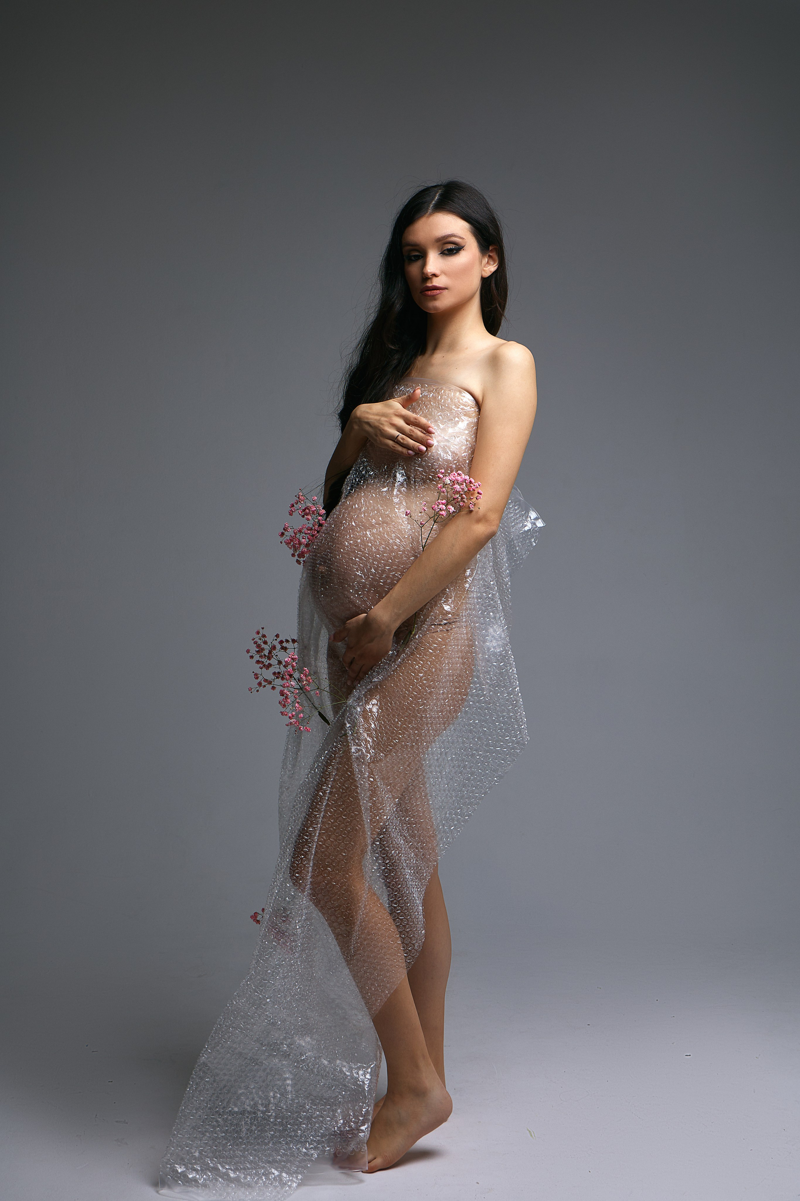 Беременная девушка в фотостудии в пленке и цветах