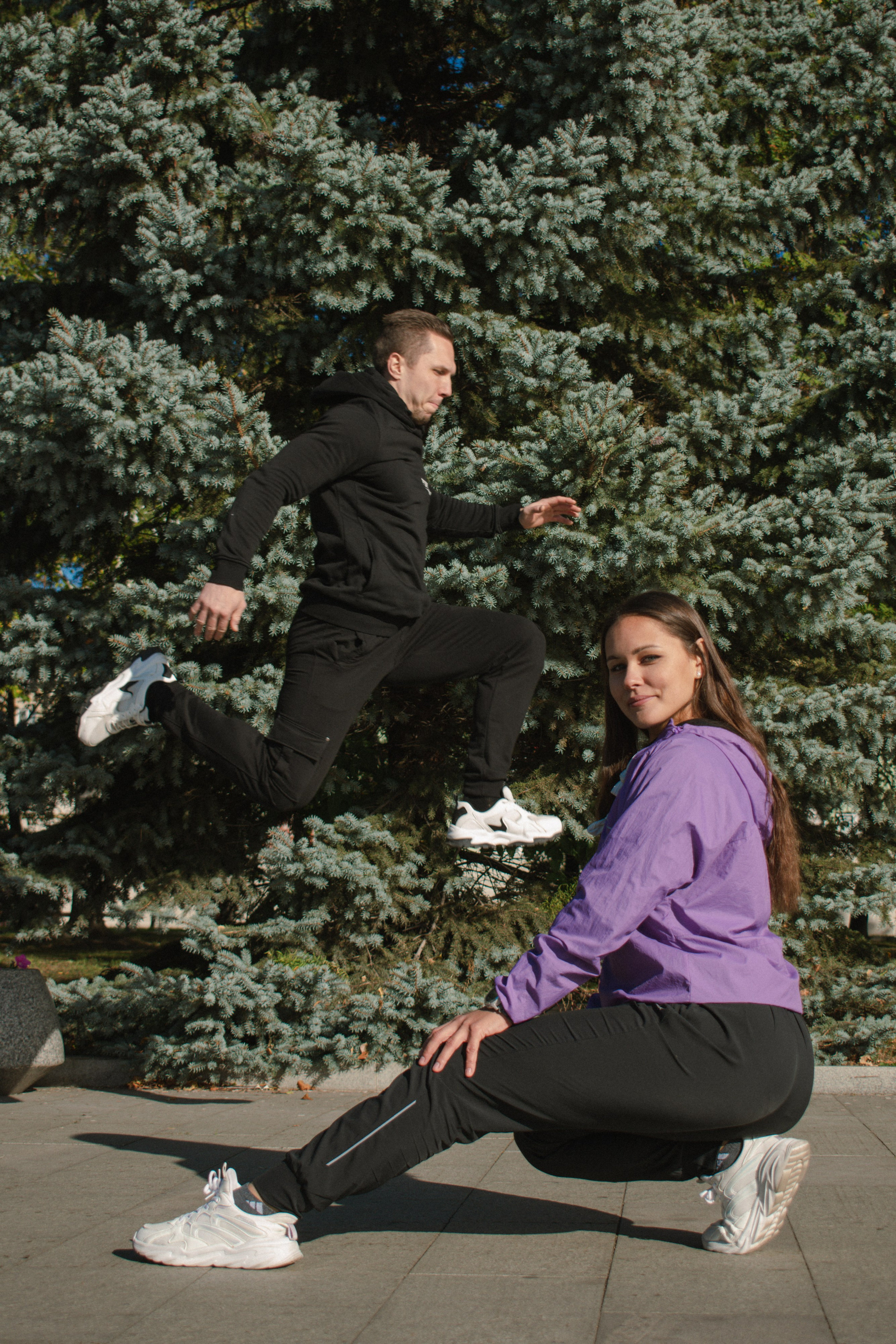 Девушка красиво сидит, а на фоне ее парень очень высоко прыгает