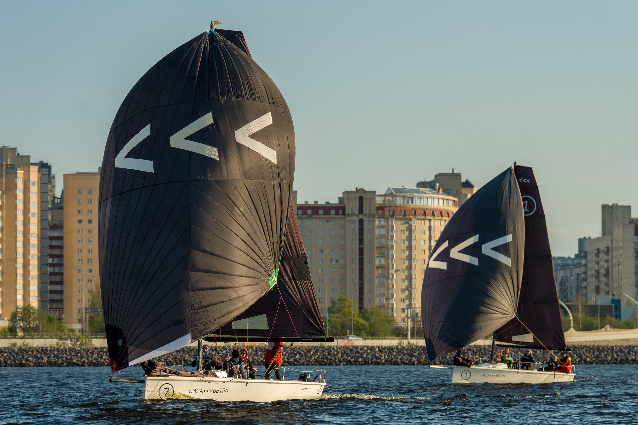 Two SV20s run under black spinnakers along the city shoreline