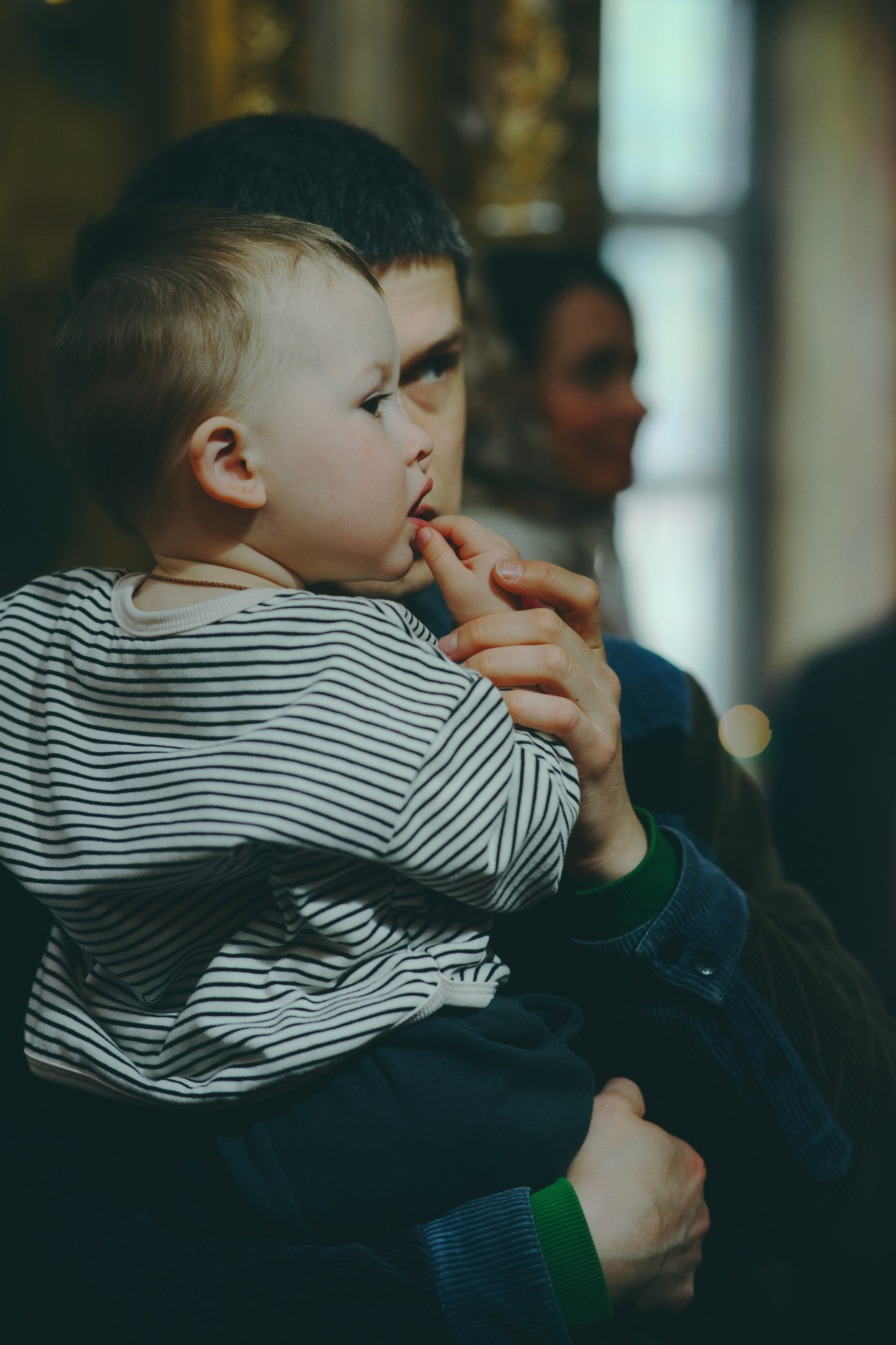 Крупный план: мужчина бережно держит малыша в полосатой кофточке. Ребёнок задумчиво смотрит в сторону, палец во рту.