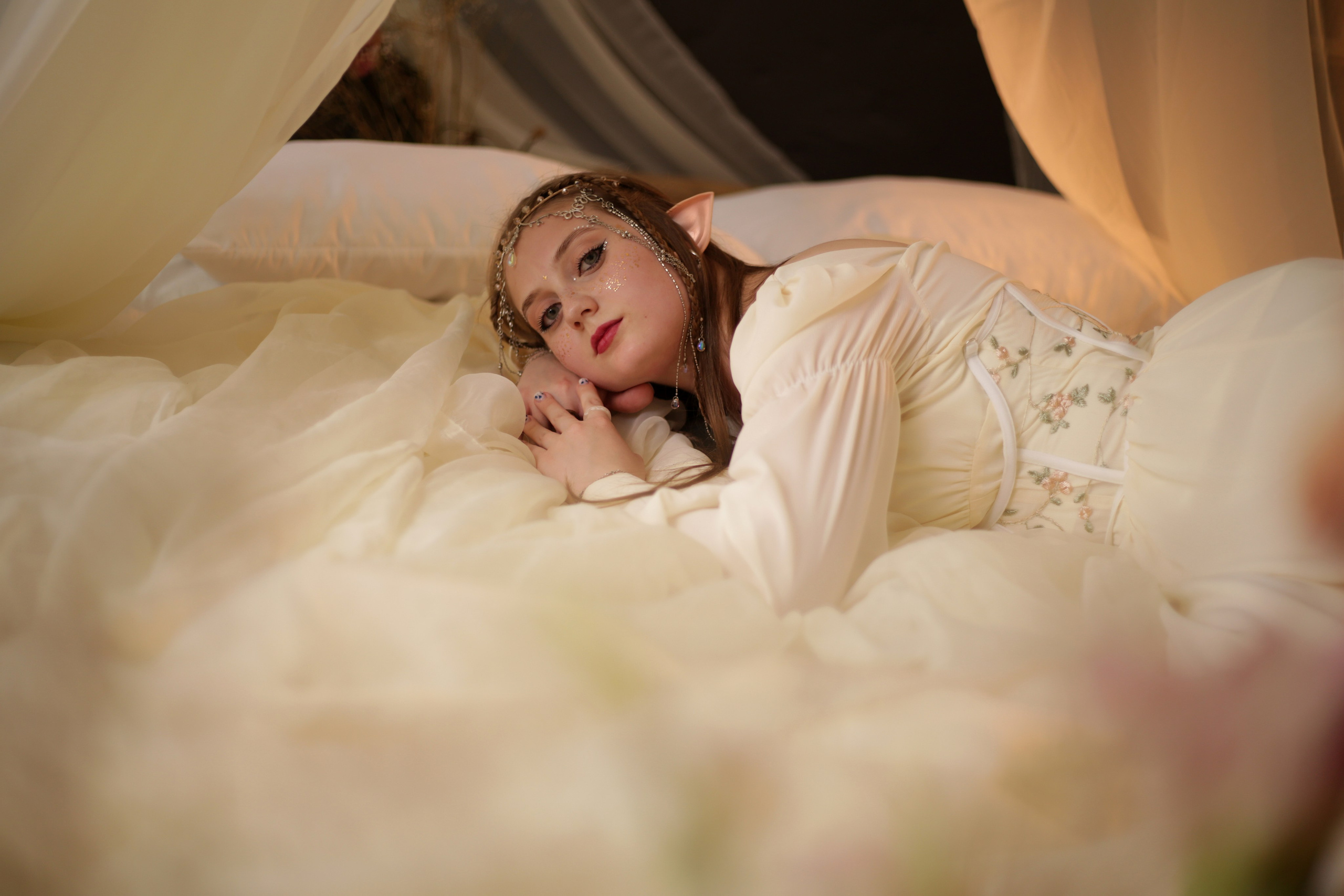 Тематическая фотосессия в Перми: девушка в белом платье спит на кровати под балдахином, лицо украшено блестками