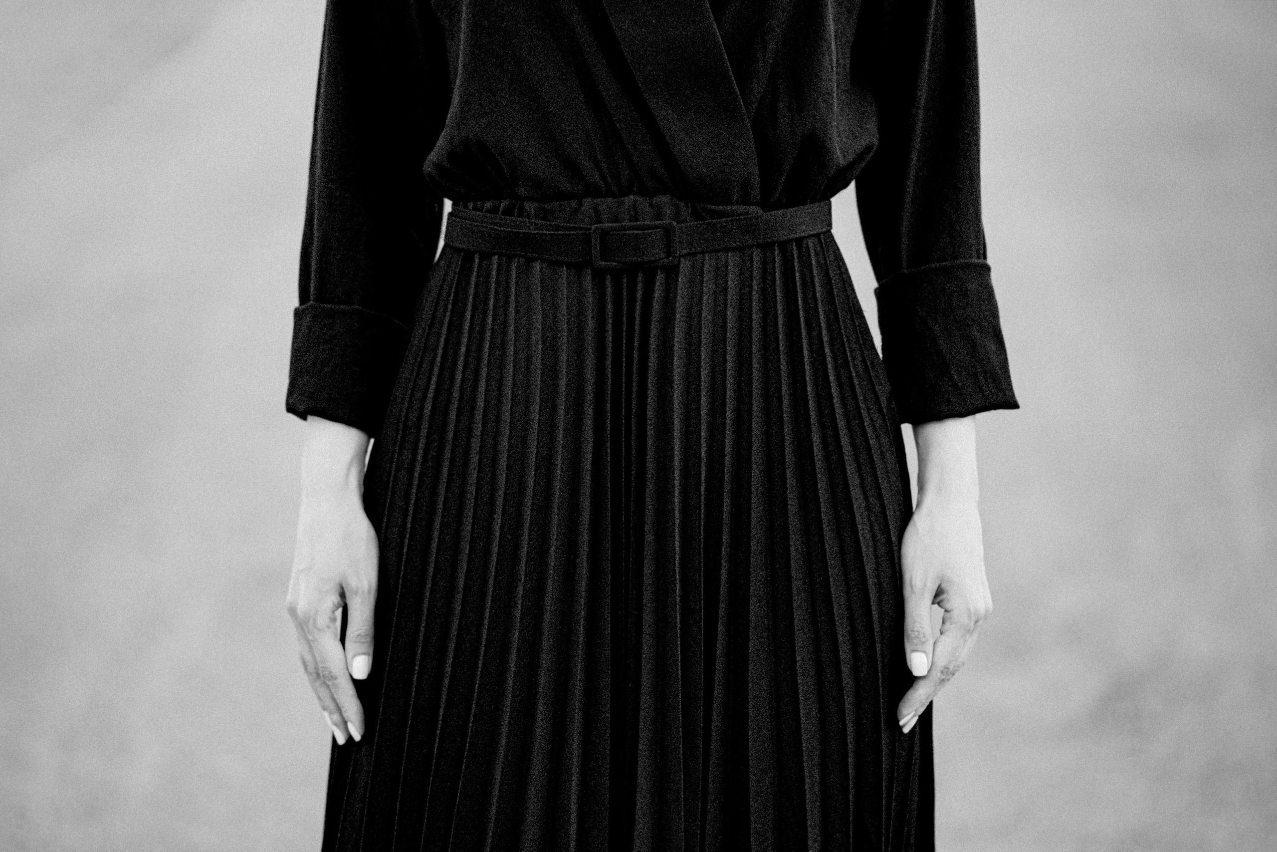 Крупный чёрно-белый кадр женских рук и чёрного плиссированного платья, минималистичная художественная композиция