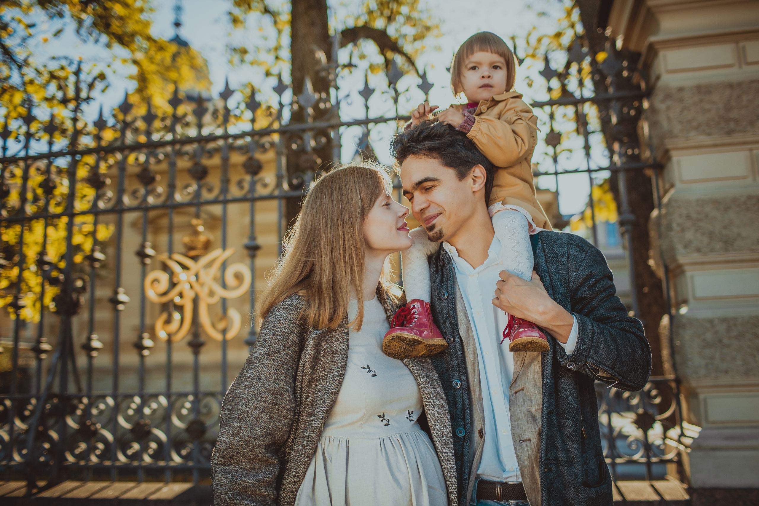 папа с маленькой дочкой на плечах целует жену на фоне решетки ограды Алексеевского дворца 