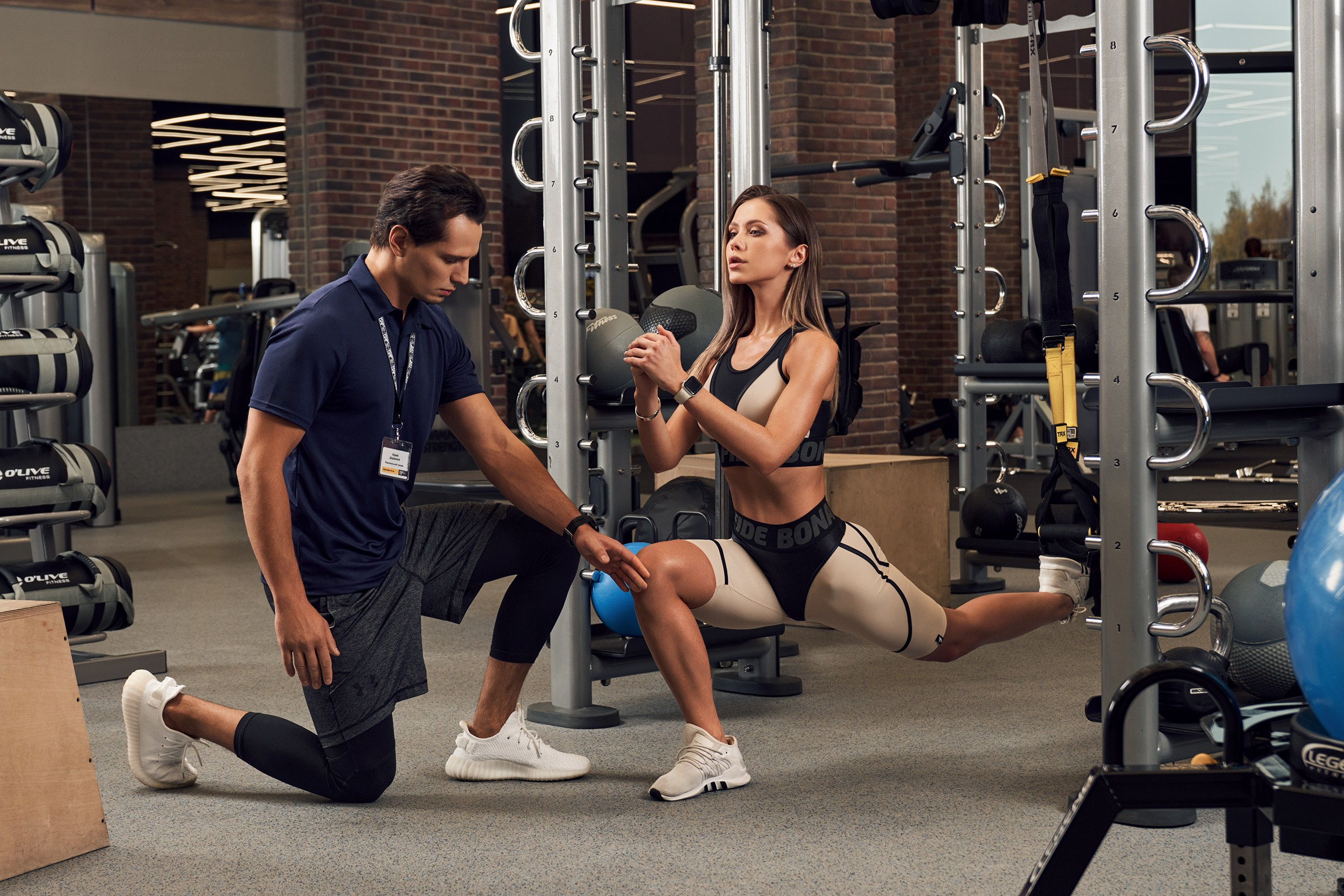 Красивая девушка занимается спортом в зале под присмотром профессионального тренера Sportlife