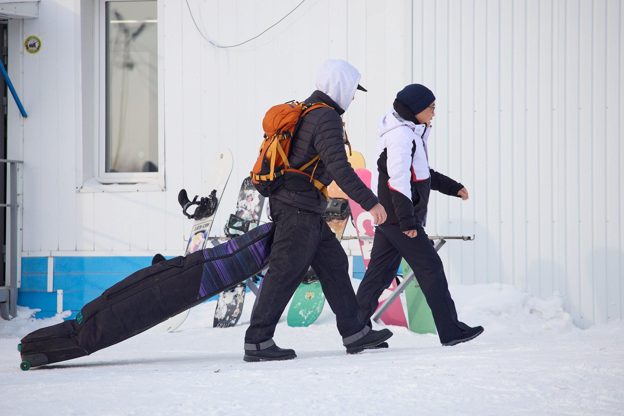 Два человека из группы поддержки несут чехол со сноубордом