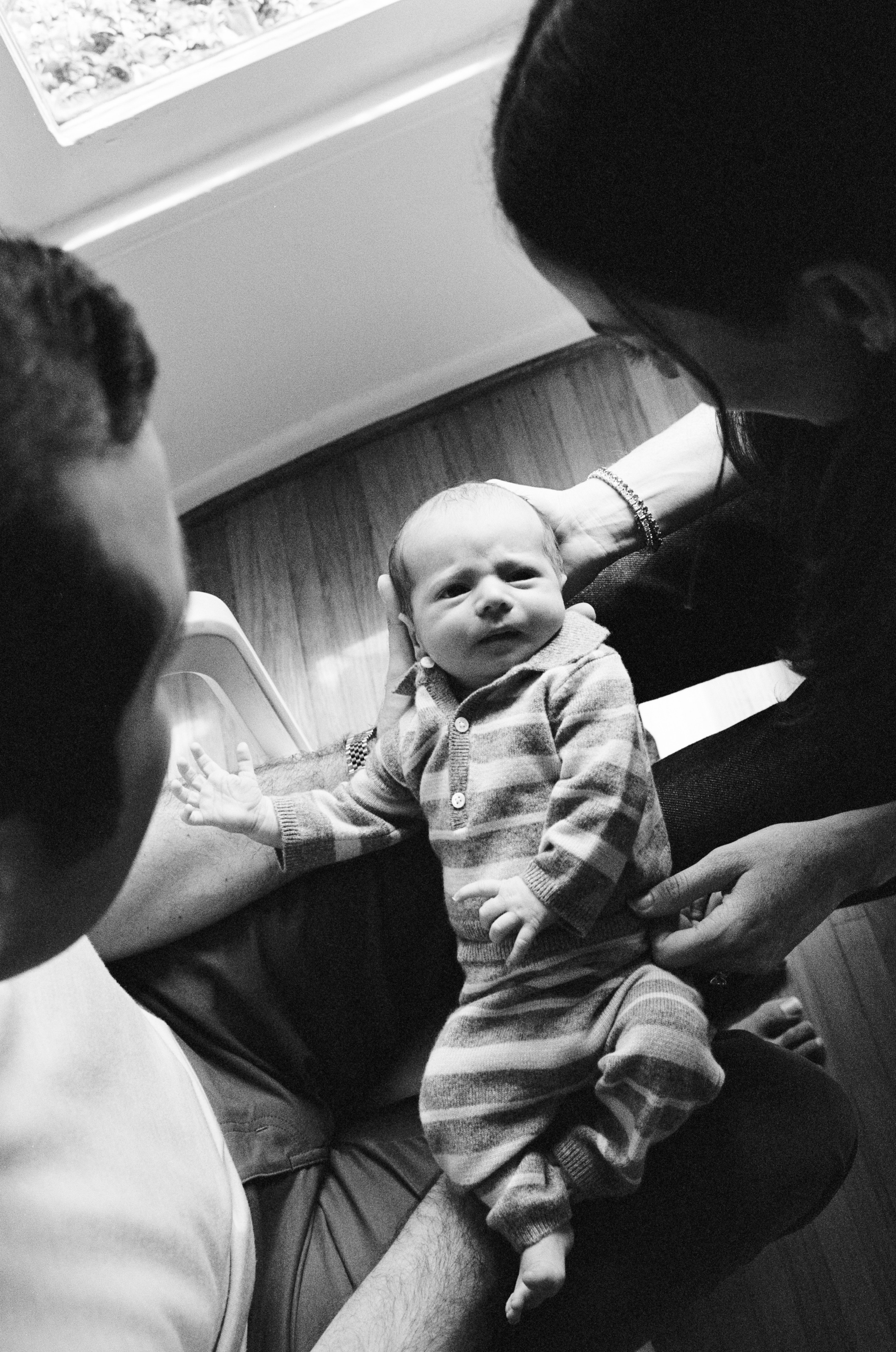 In the middle of a black and white film photo is a baby, held by both sides by his parents