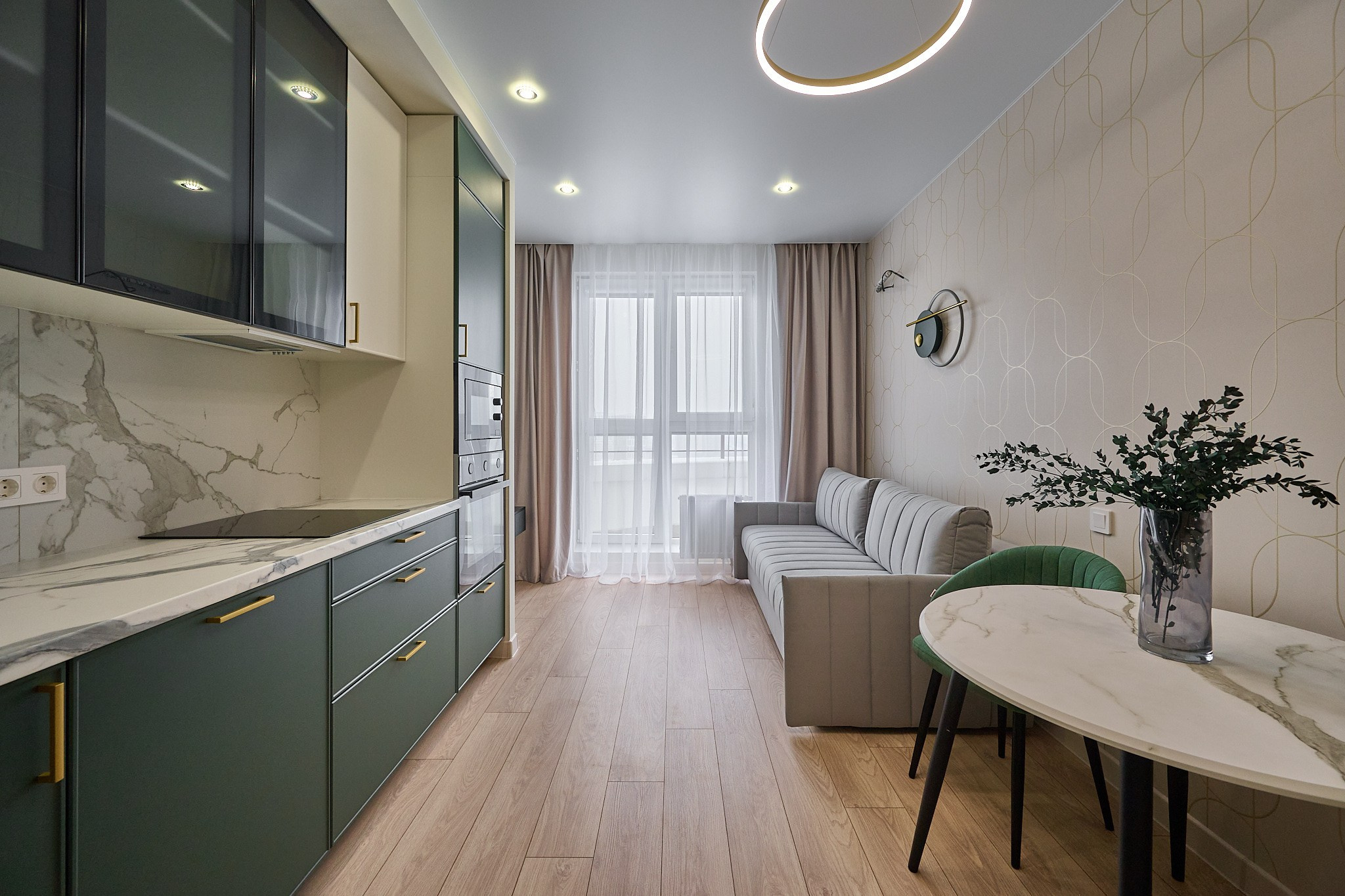 кухня темно зеленые шкафы  белый кухонный стол и светлый диван  светлые шторы 