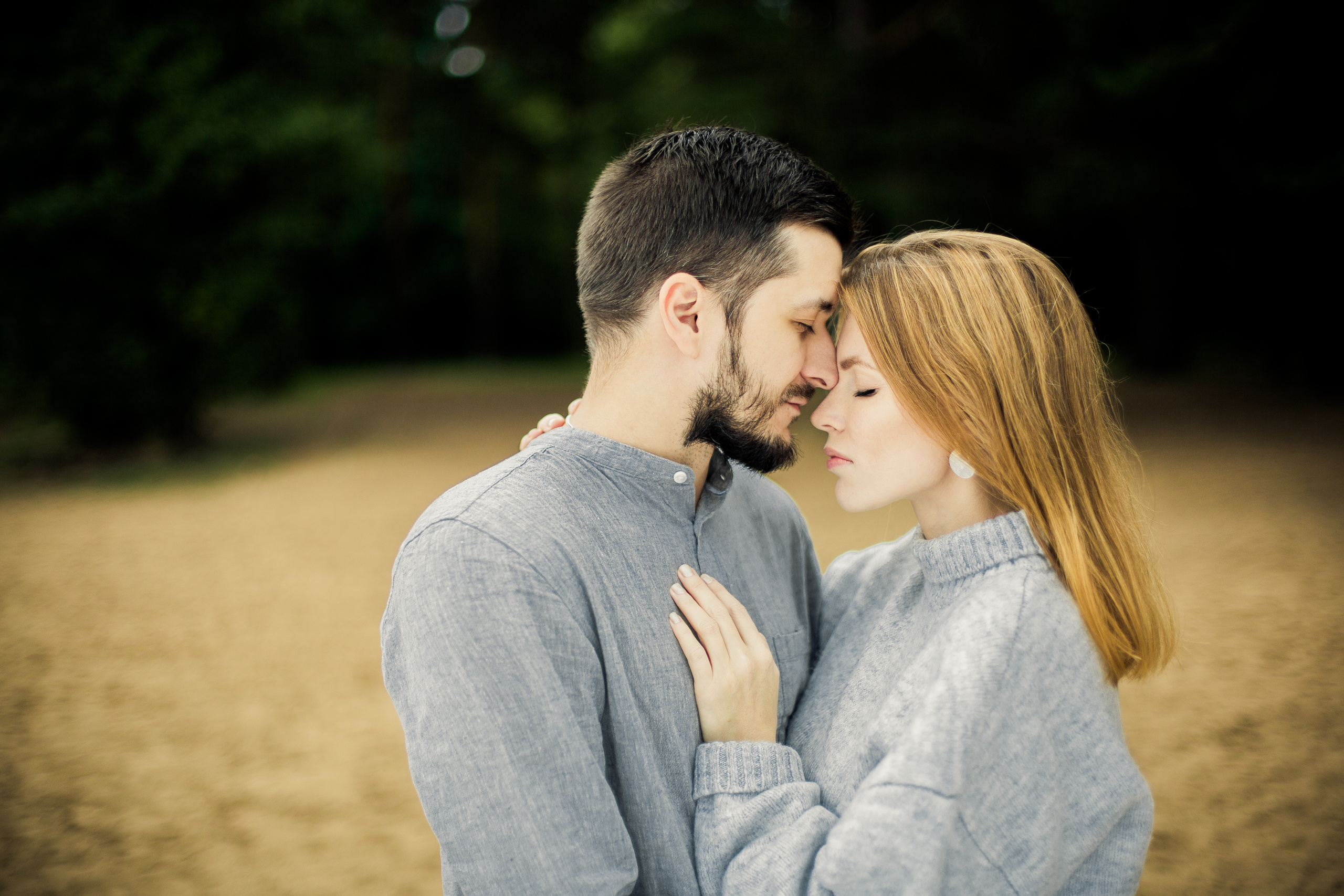 нежное прикосновение лбами влюбленных в серых свитере и рубашке на пляже