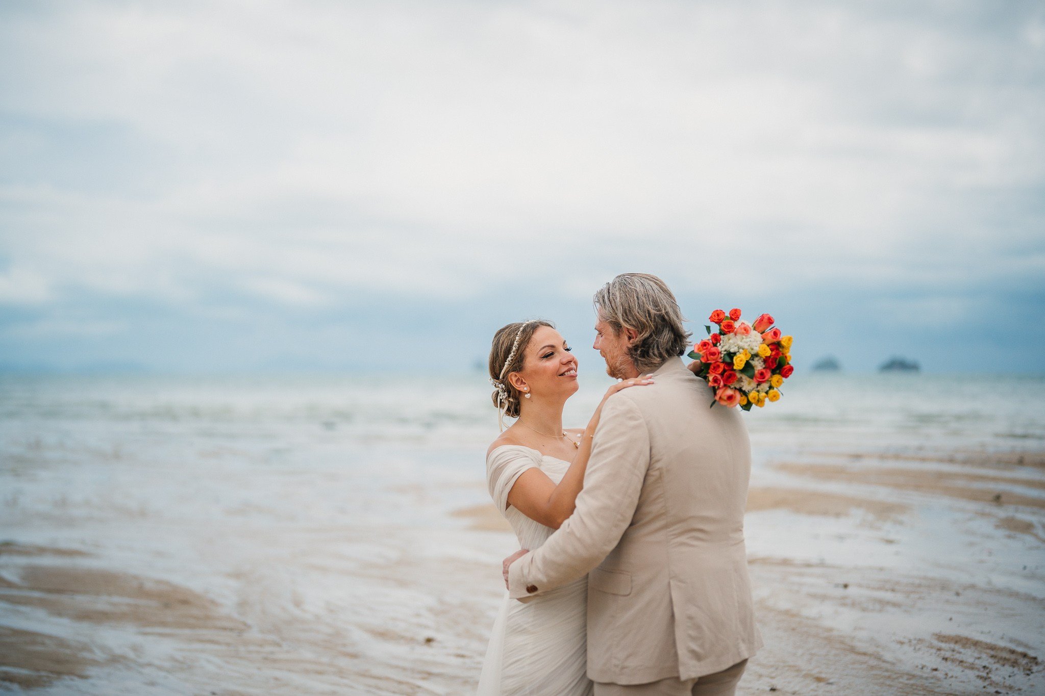 Couple taking part in a traditional Buddhist wedding ceremony on a tropical beach in Koh Samui, Thailand, with monks, flowers, and ocean views.