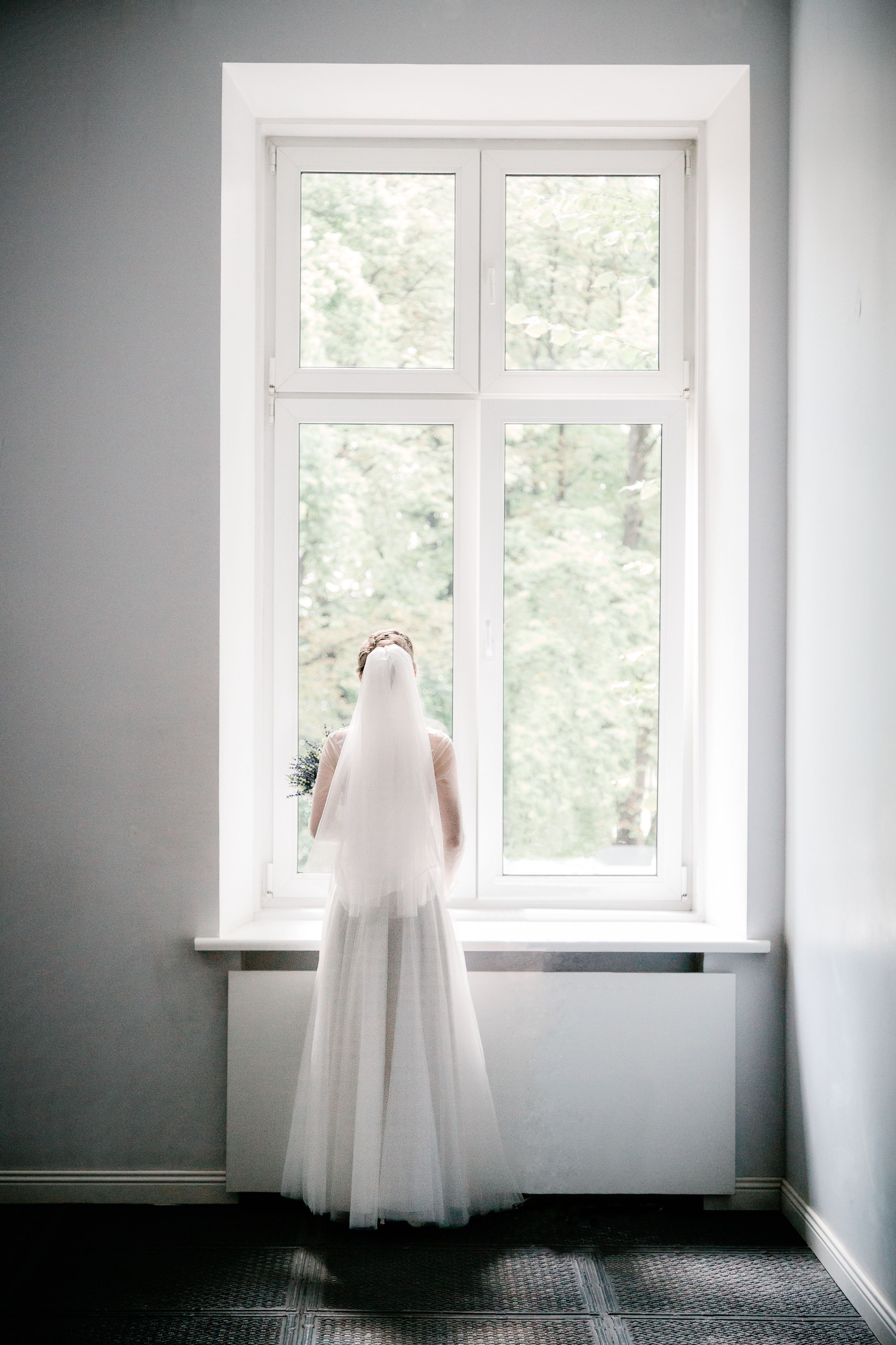 невеста в свадебном платье смотрит в окно