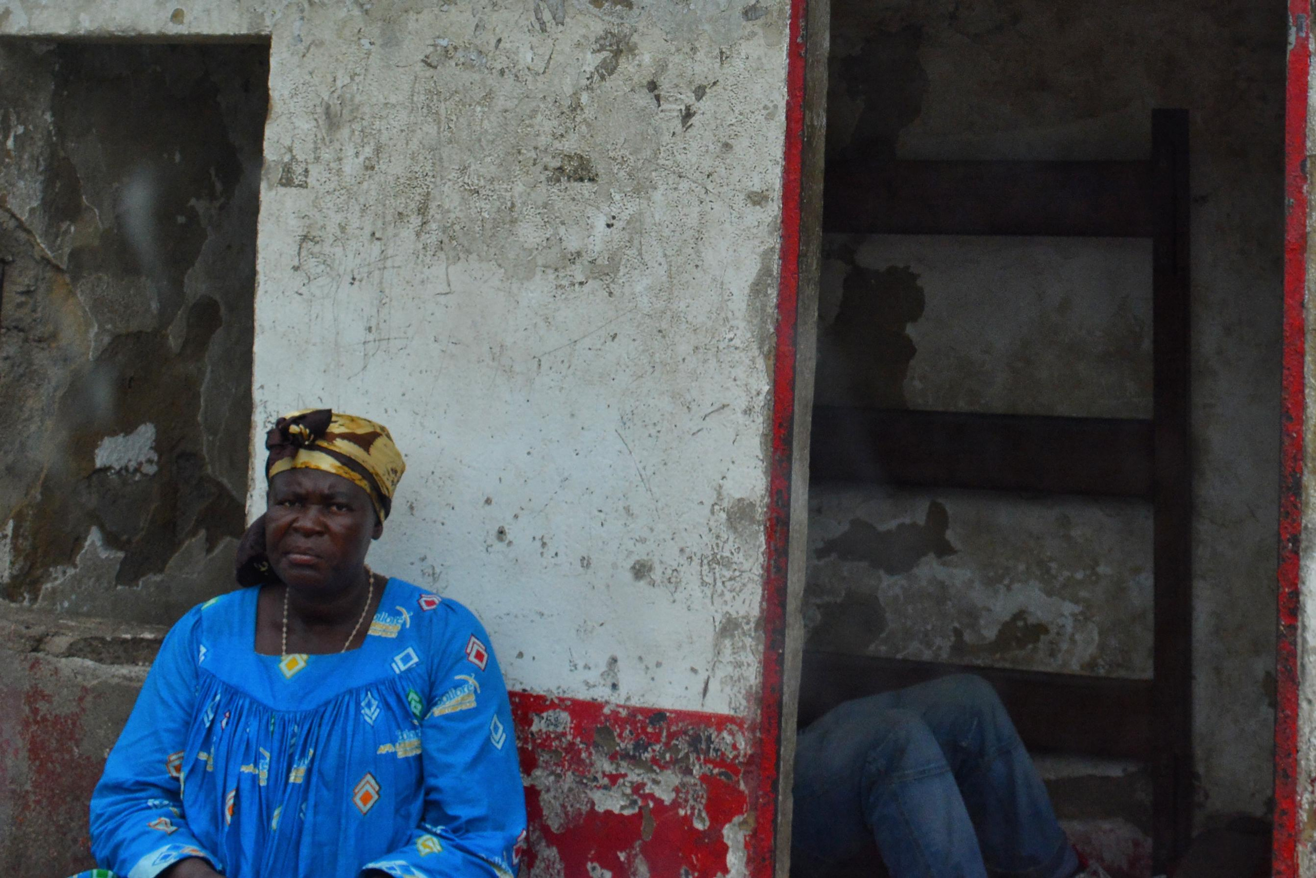 Темнокожая женщина в синем сидит на автобусной остановке, Камерун, Camerun