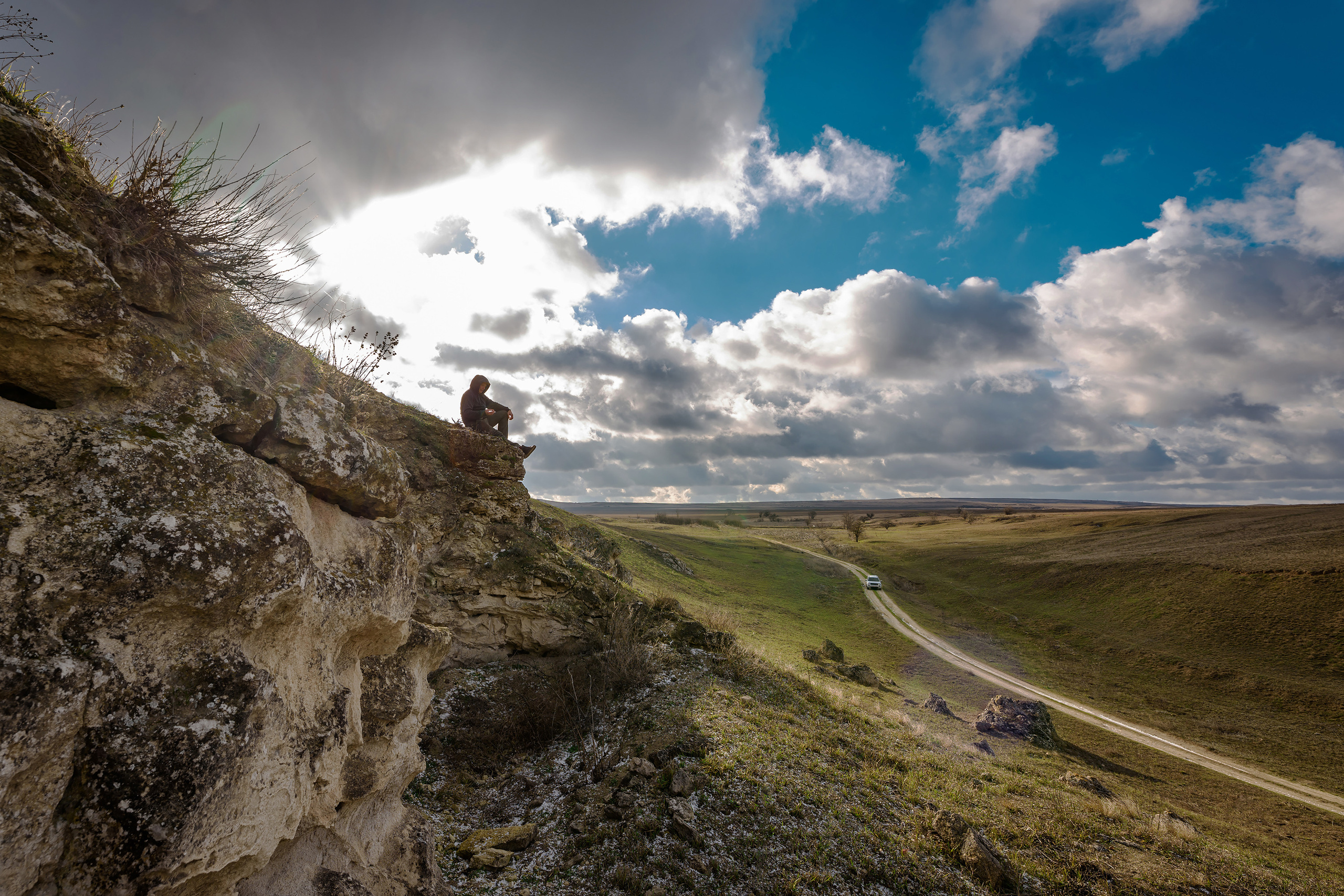 Мужчина сидит на скале над дорогой