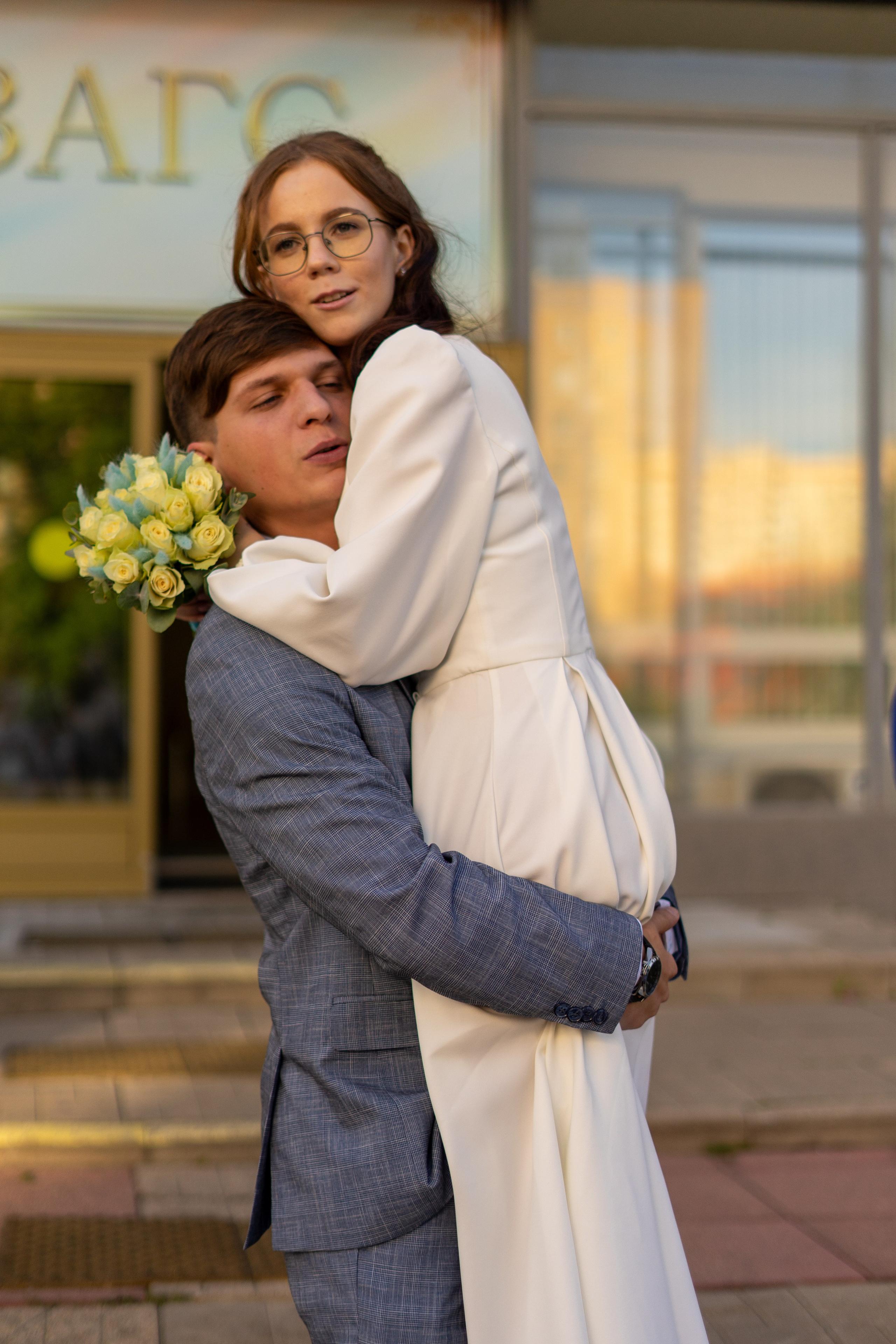 Жених держит на руках свою жену у дверей загса